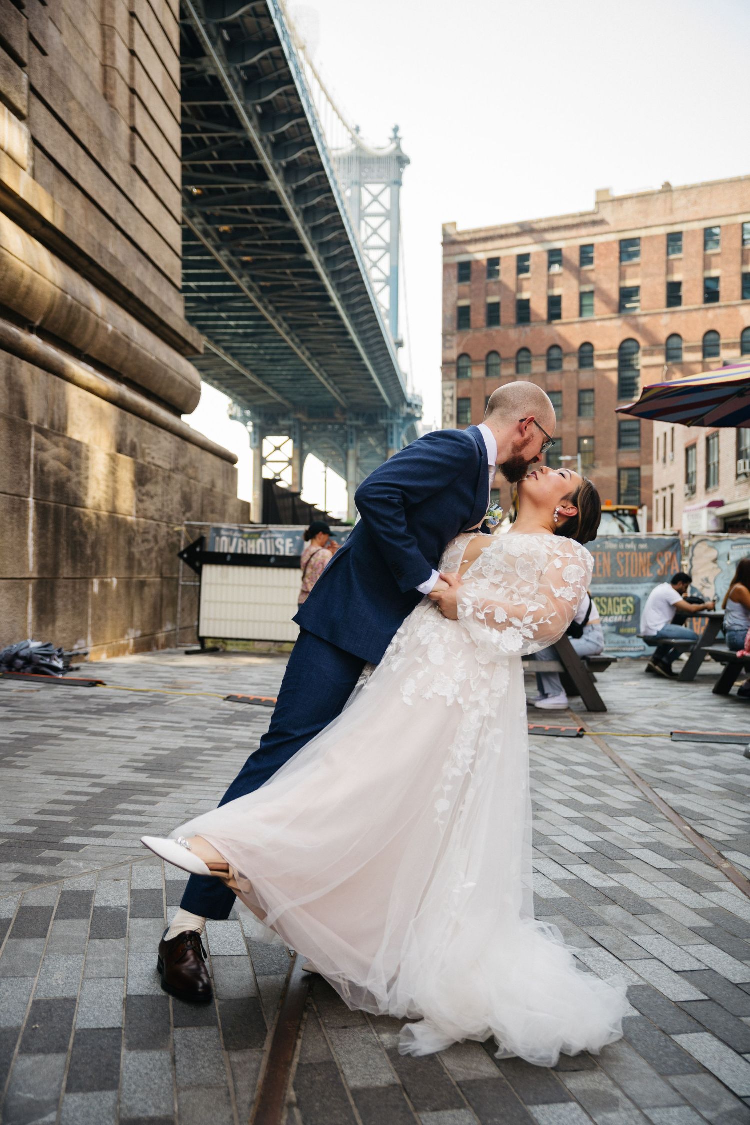 Bride and groom share a romantic dip kiss in DUMBO Brooklyn with Manhattan Bridge backdrop.