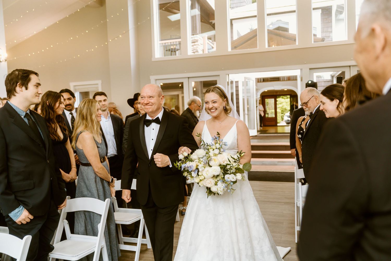 Bride walks down the aisle with her father during an elegant indoor wedding ceremony.
