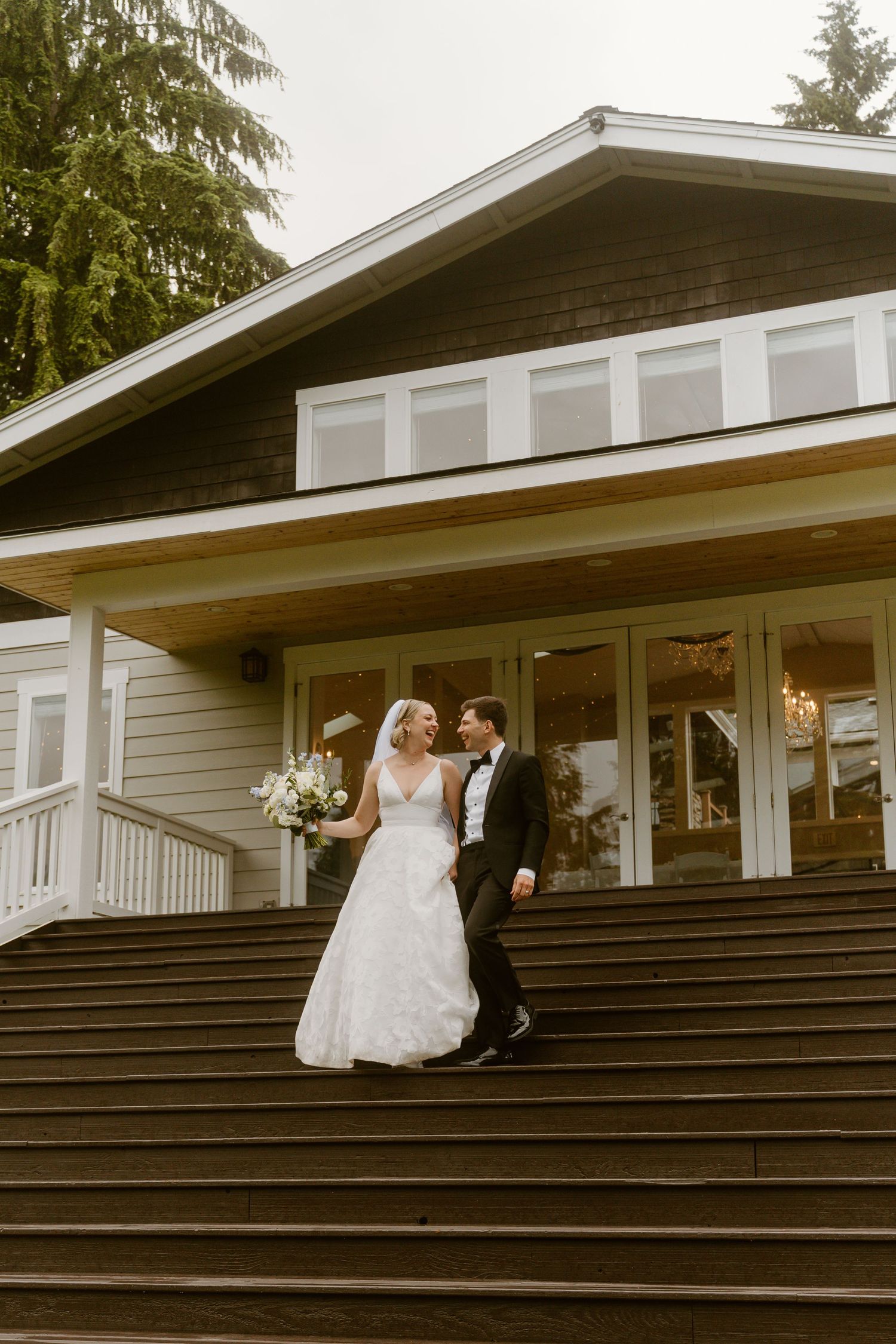 Bride and groom walking down outdoor steps of a rustic wedding venue, sharing a joyful glance.