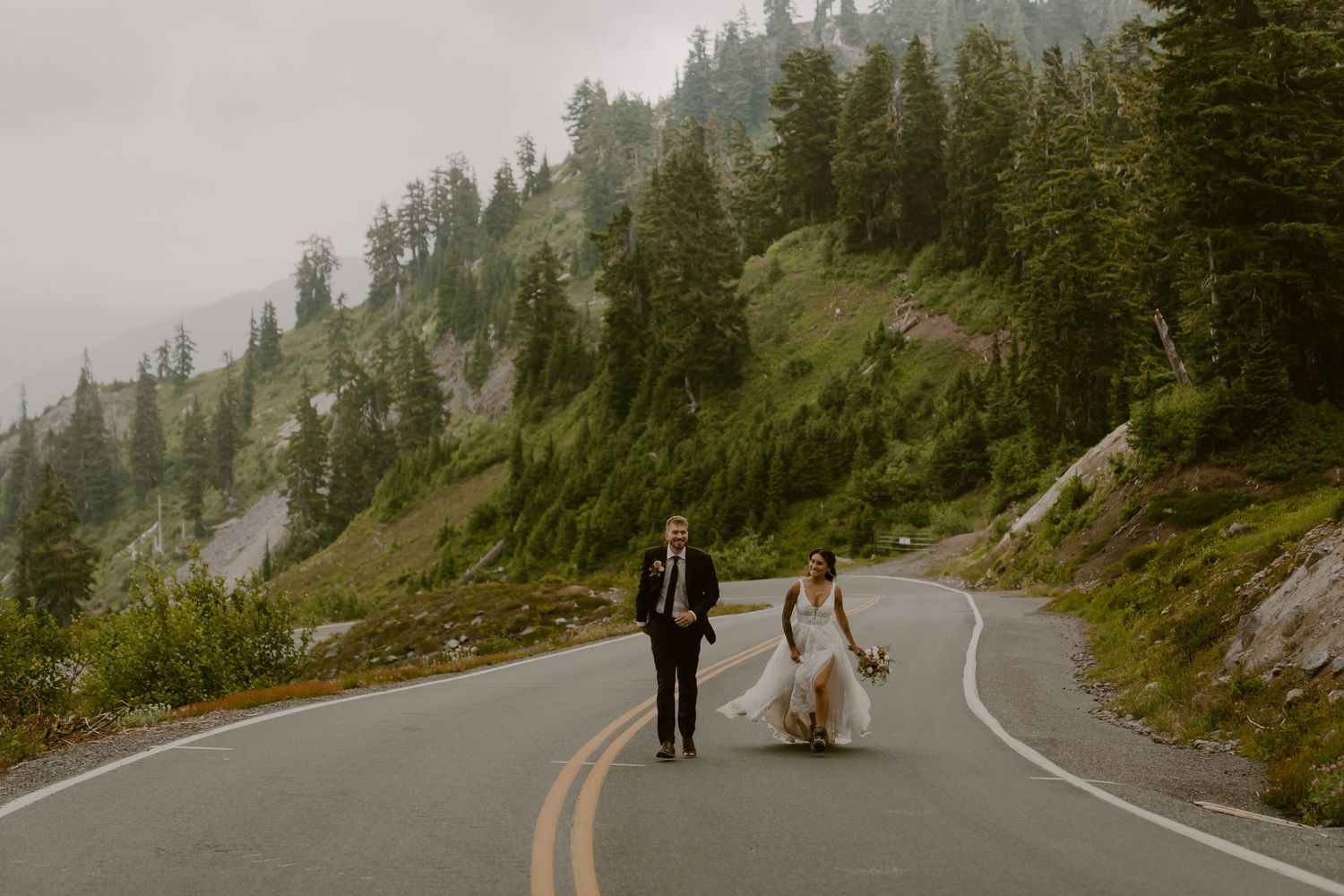 A person walks along a misty mountain road surrounded by evergreen trees on a foggy morning.
