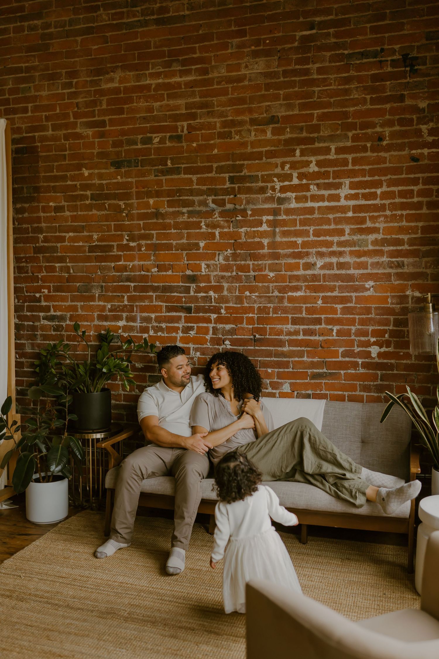 Couple sharing an intimate moment on a couch against exposed brick wall with potted plants in an industrial loft space.