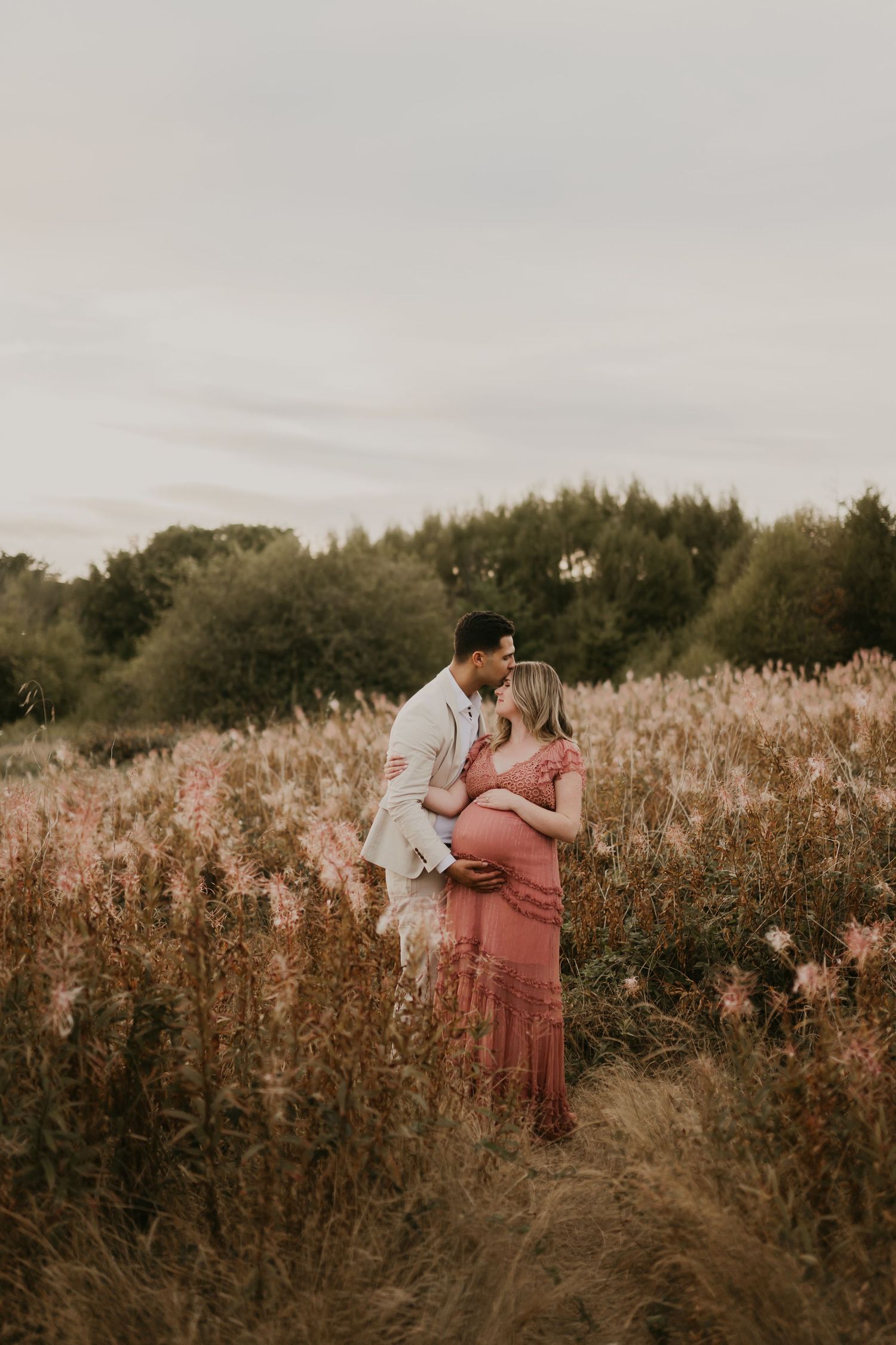 Couple sharing a tender kiss in a golden field during a maternity photo session at sunset.