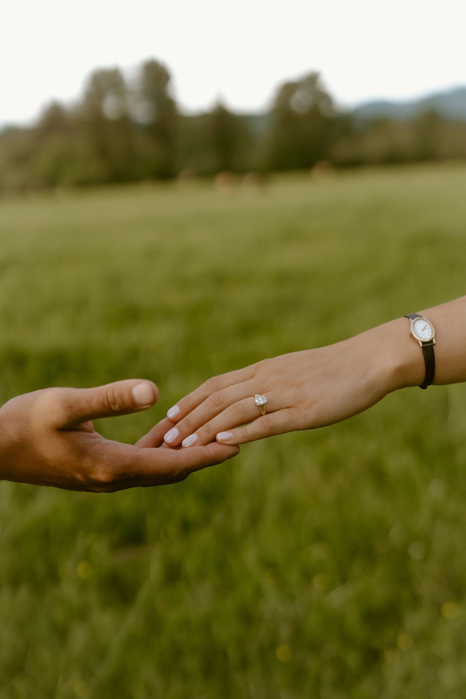 Close-up of two hands reaching toward each other, womans hand wearing an engagement ring and watch.