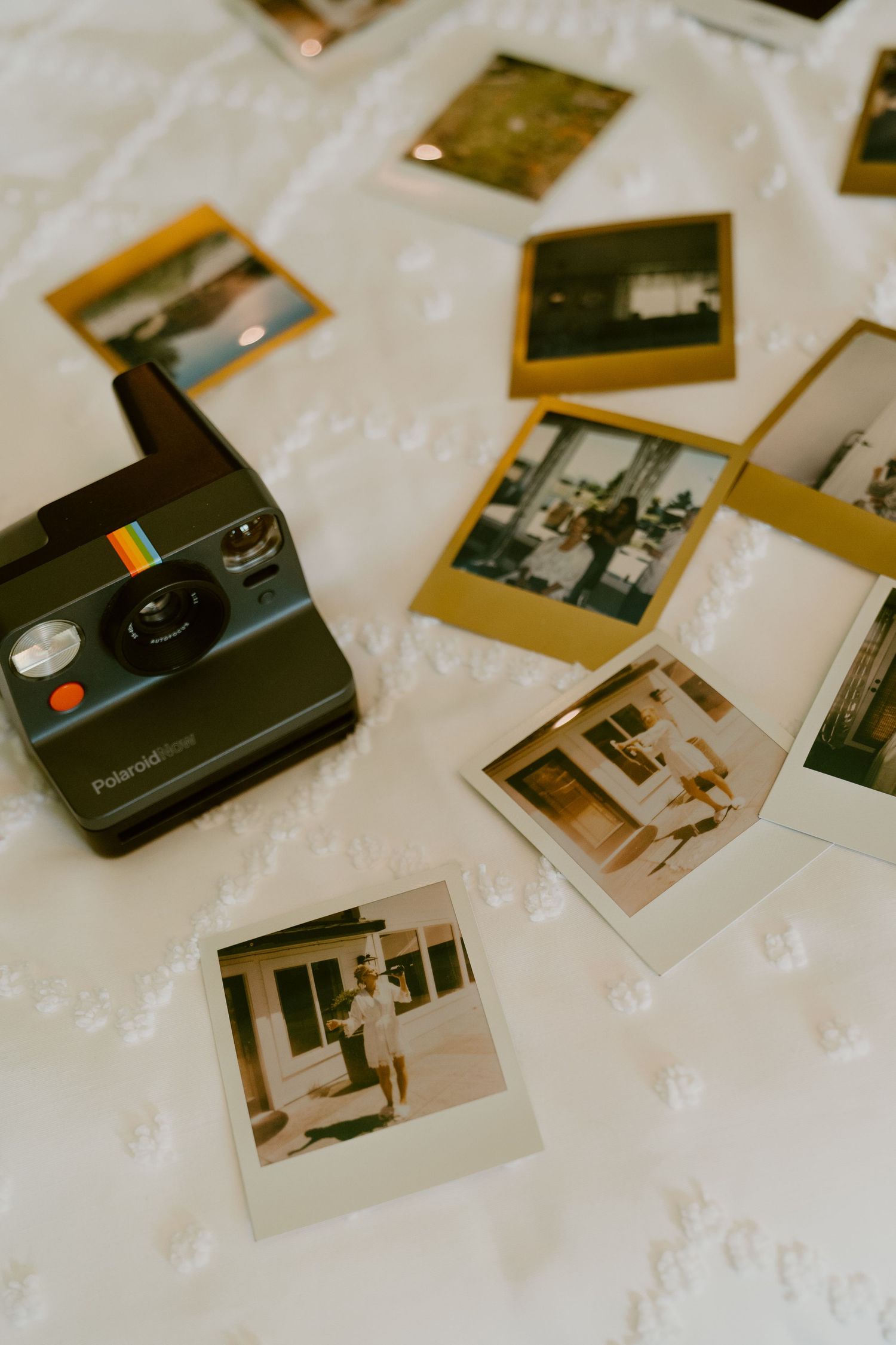 Vintage Polaroid camera and scattered instant photo prints arranged on a white textured surface.