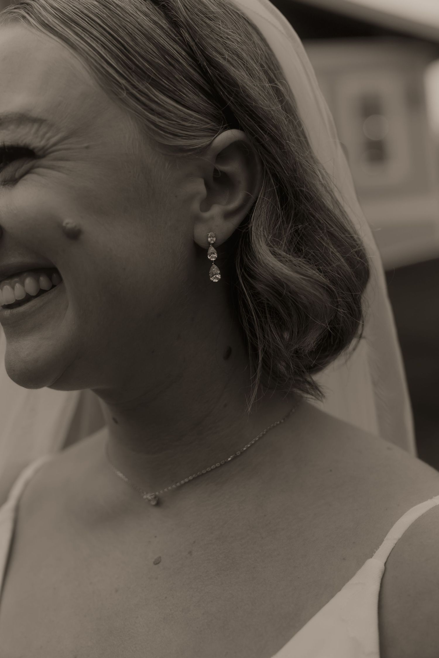 Black and white close-up of bride smiling, wearing elegant drop crystal earrings and delicate necklace.