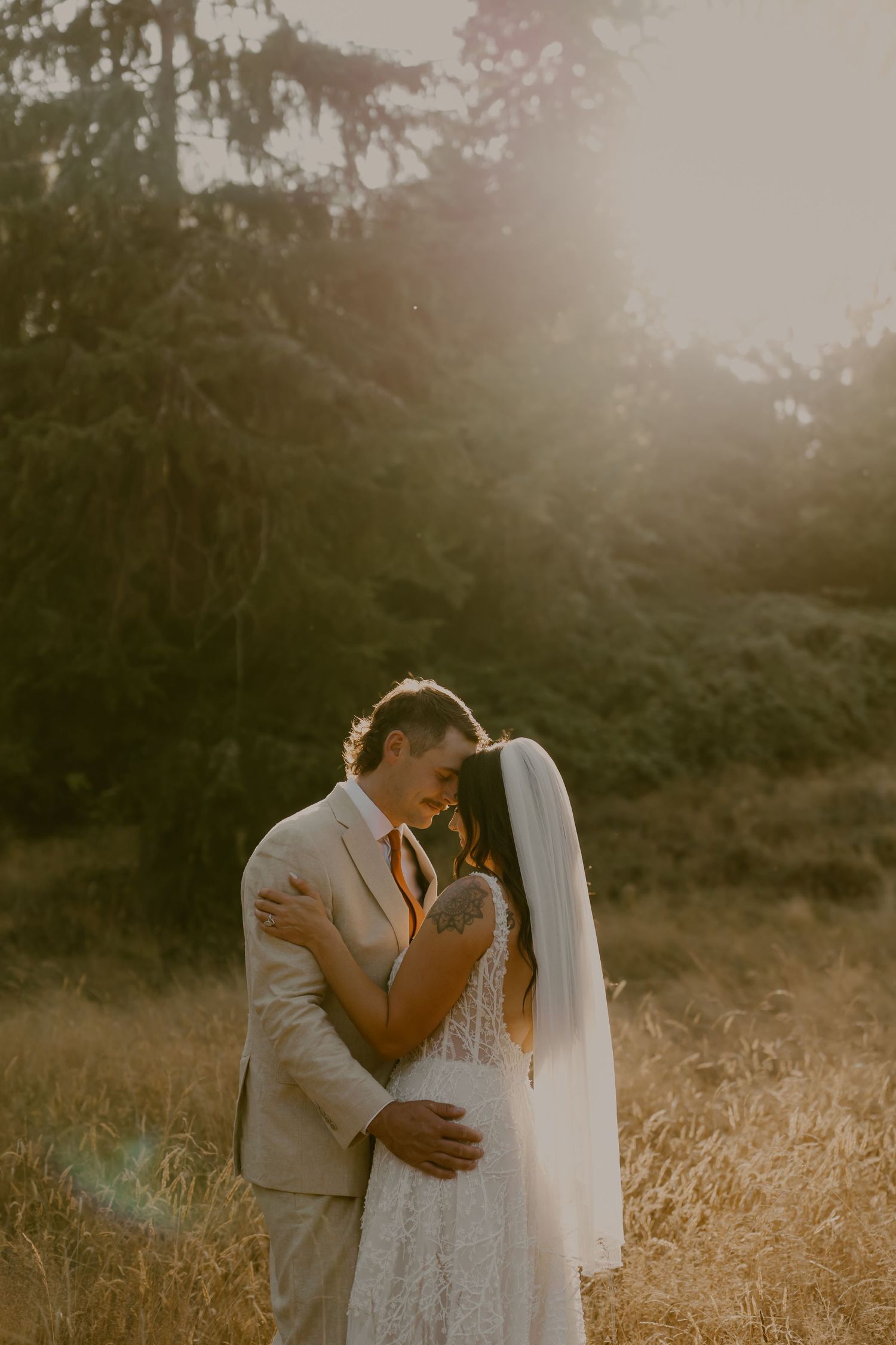 A romantic sunset wedding photo shows a couple embracing in a golden field with misty evergreen trees in the background.