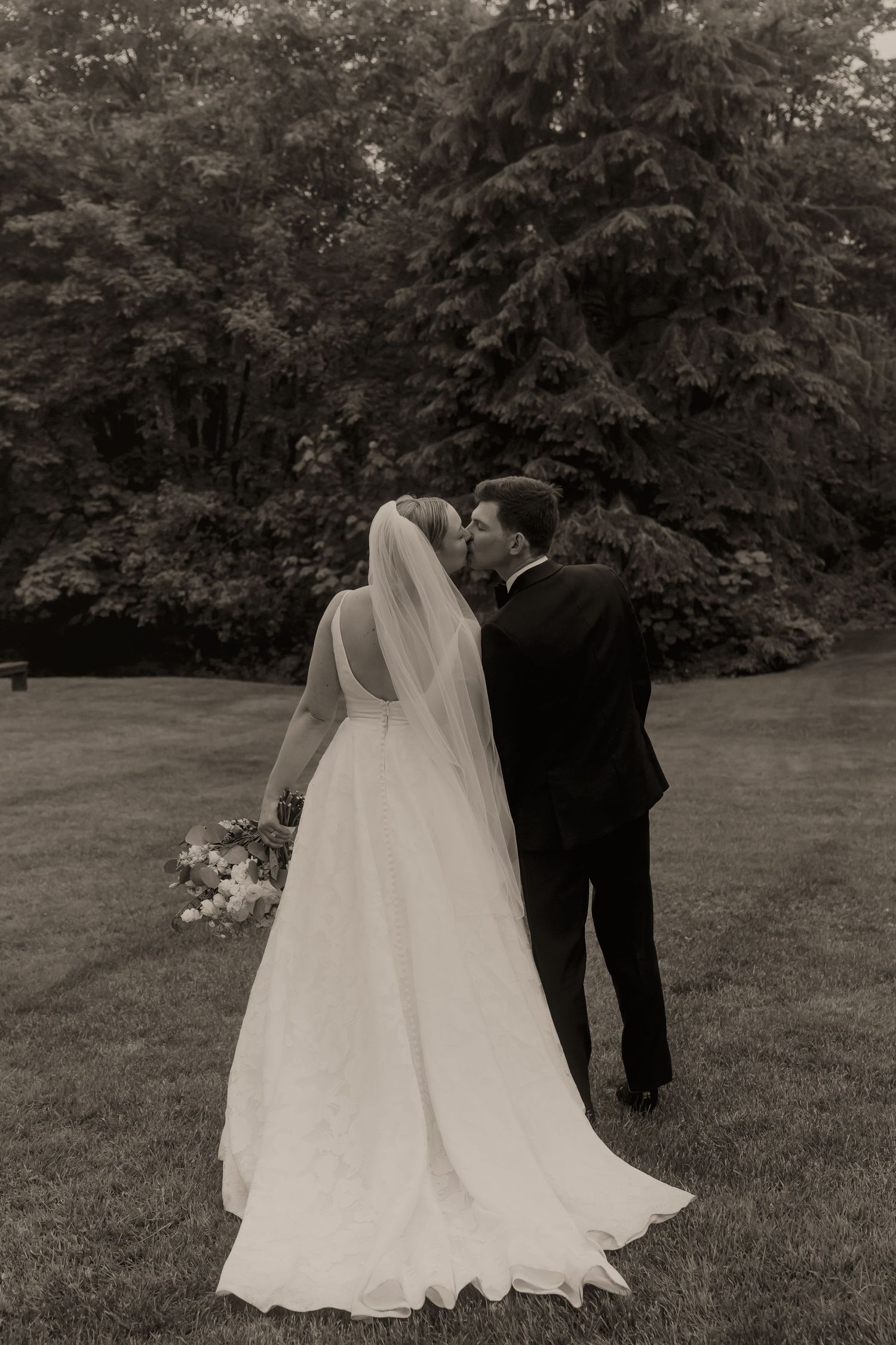 Black and white photo of bride and groom sharing a tender kiss in a lush garden.