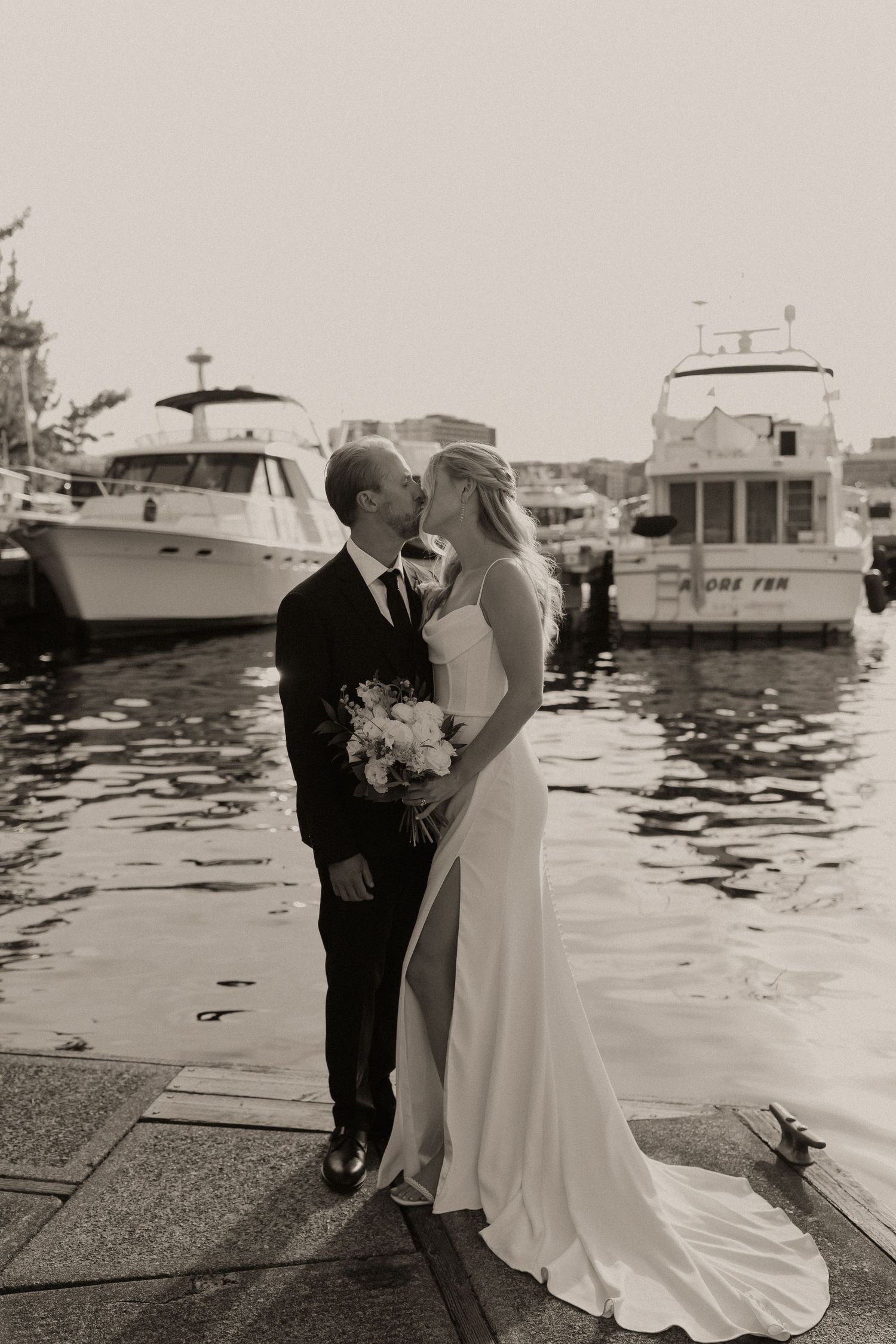 Black and white photo of bride and groom kissing on a marina dock with luxury yachts in the background.