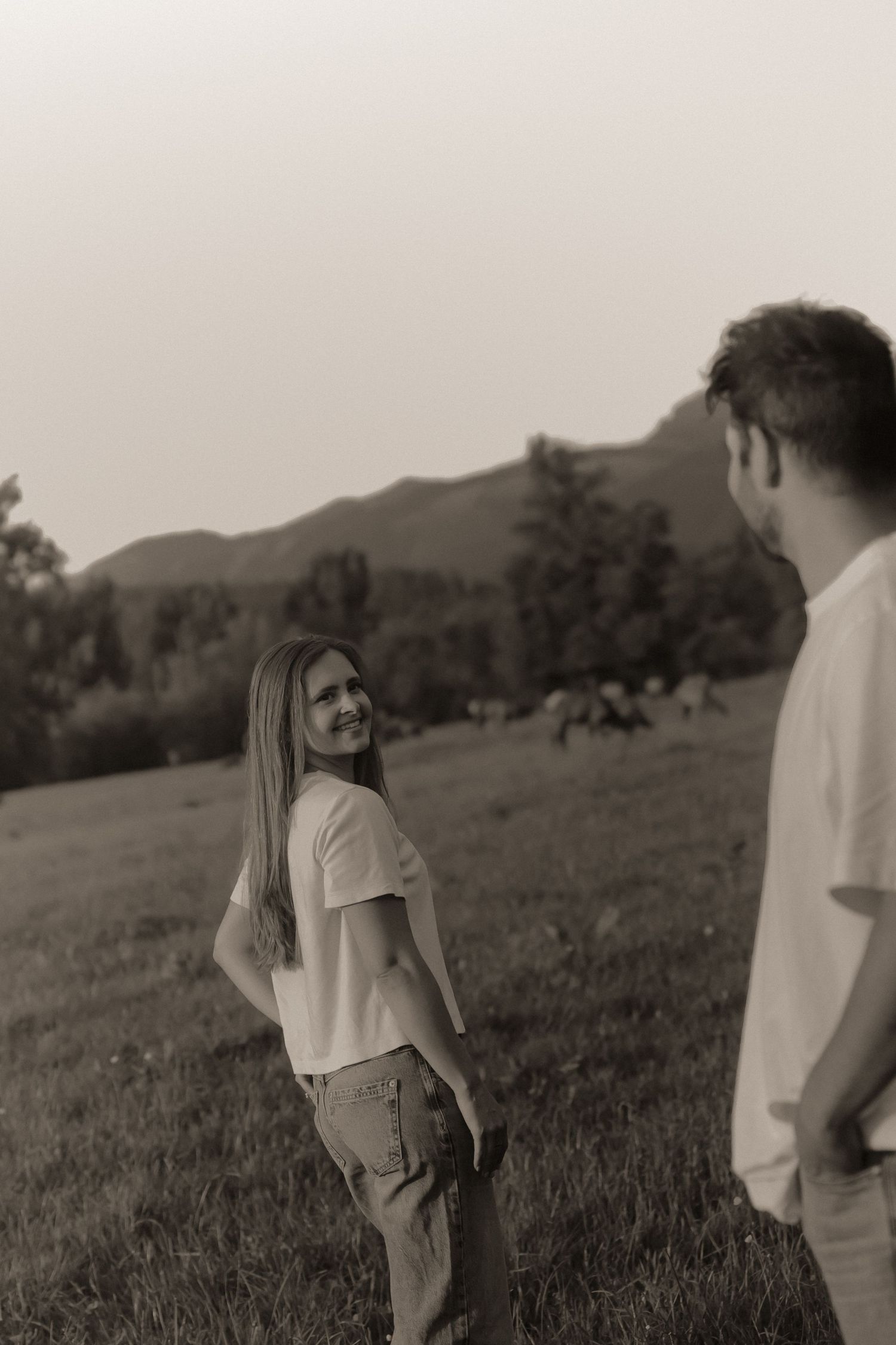 Black and white photo of a smiling woman in white t-shirt looking back at a man in a green meadow.