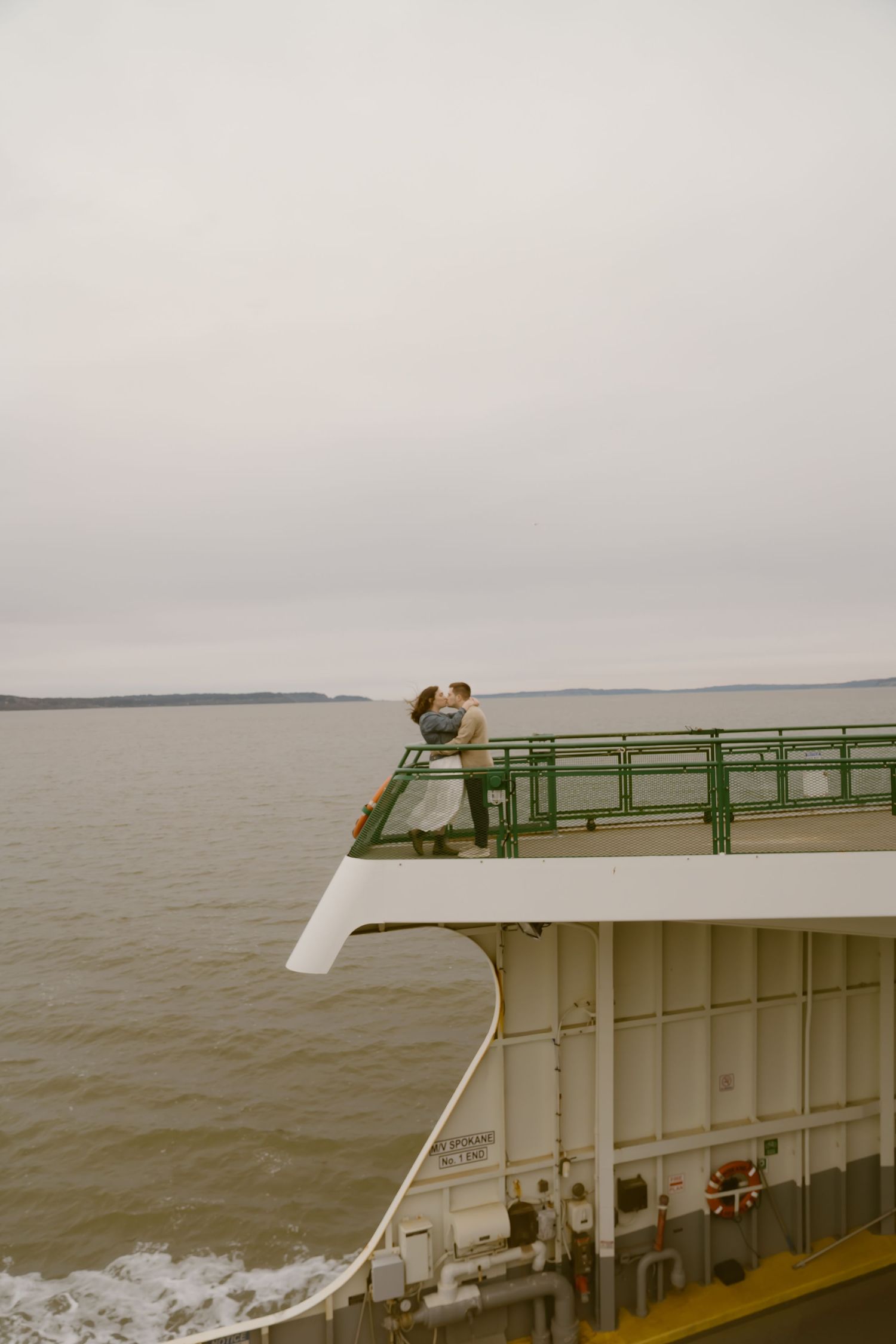 Couple kissing on the upper deck railing of a ferry boat on a calm gray overcast day on the water.