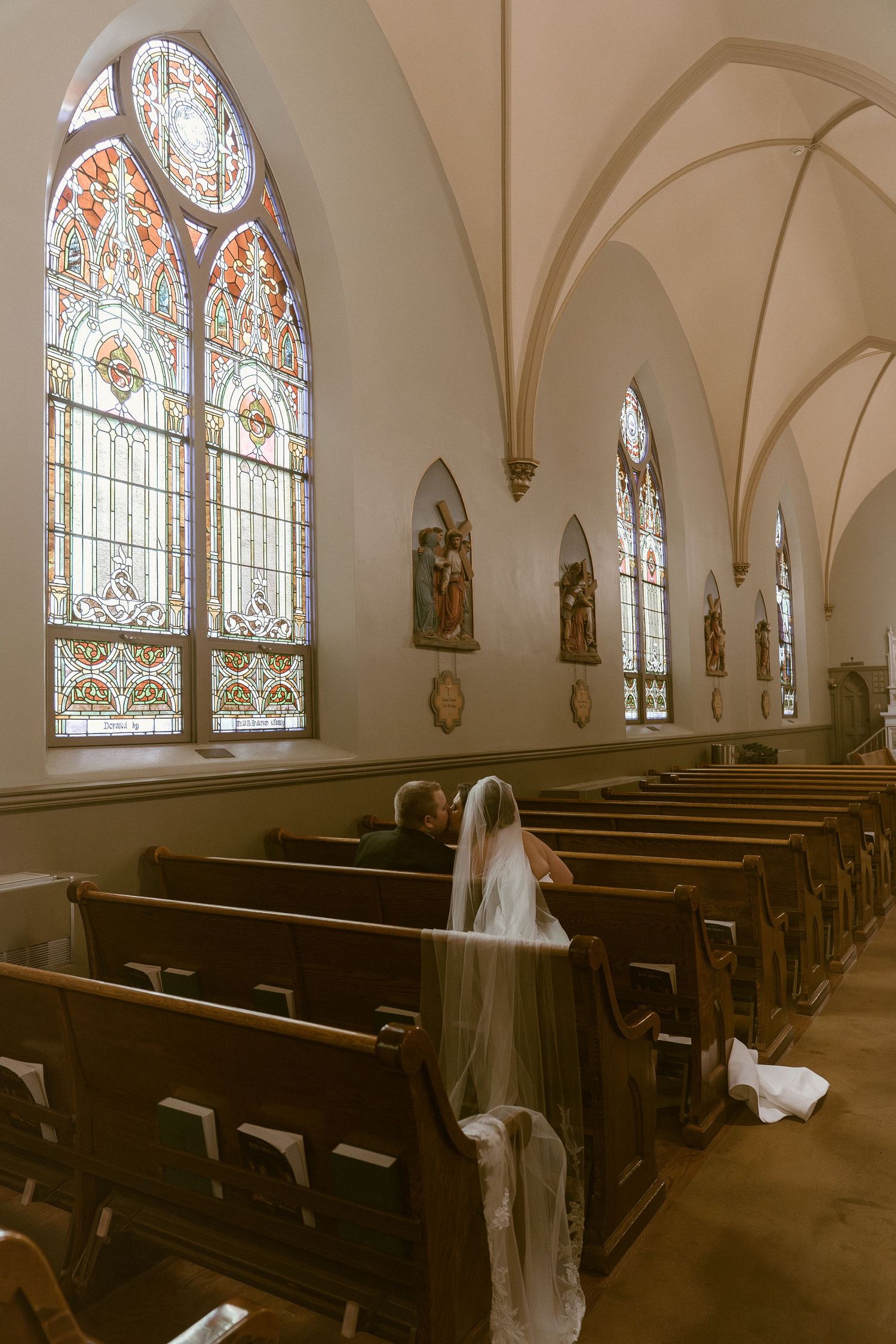 Panoramic view of a church interior with stained glass windows, wooden pews, and vaulted gothic arches.