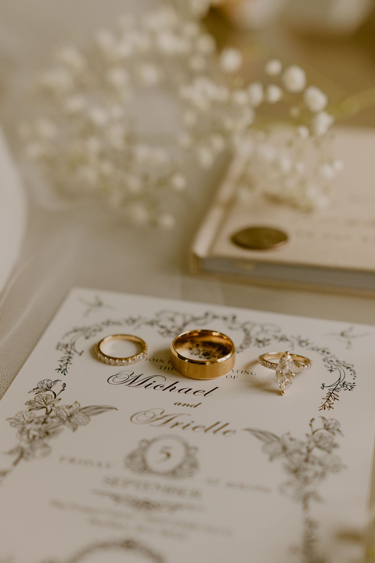 Three wedding rings displayed on an elegant wedding invitation with decorative floral border details in sepia tones.