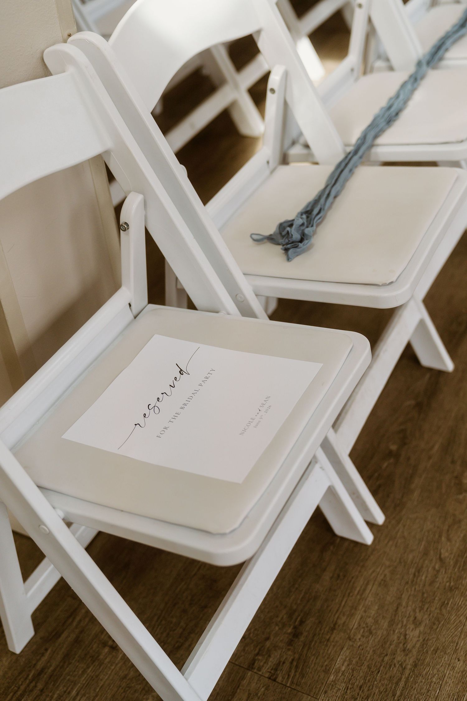 White folding chairs with reserved signs and blue ribbon at an elegant wedding ceremony.