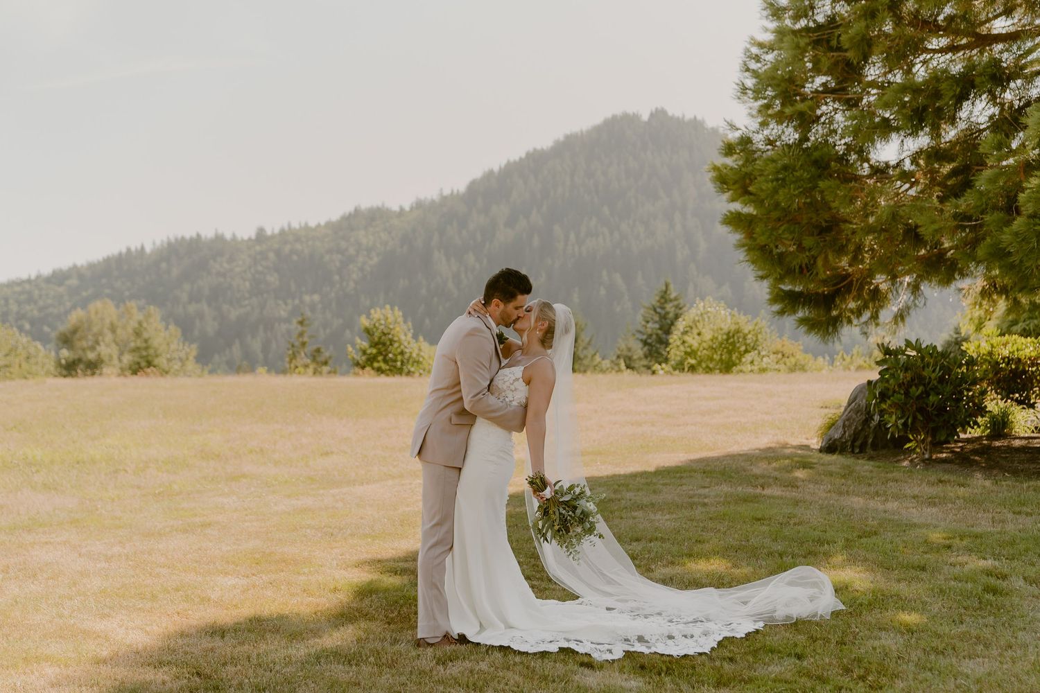 A couple shares a romantic moment at sunset on a hilltop overlooking a scenic mountain landscape.