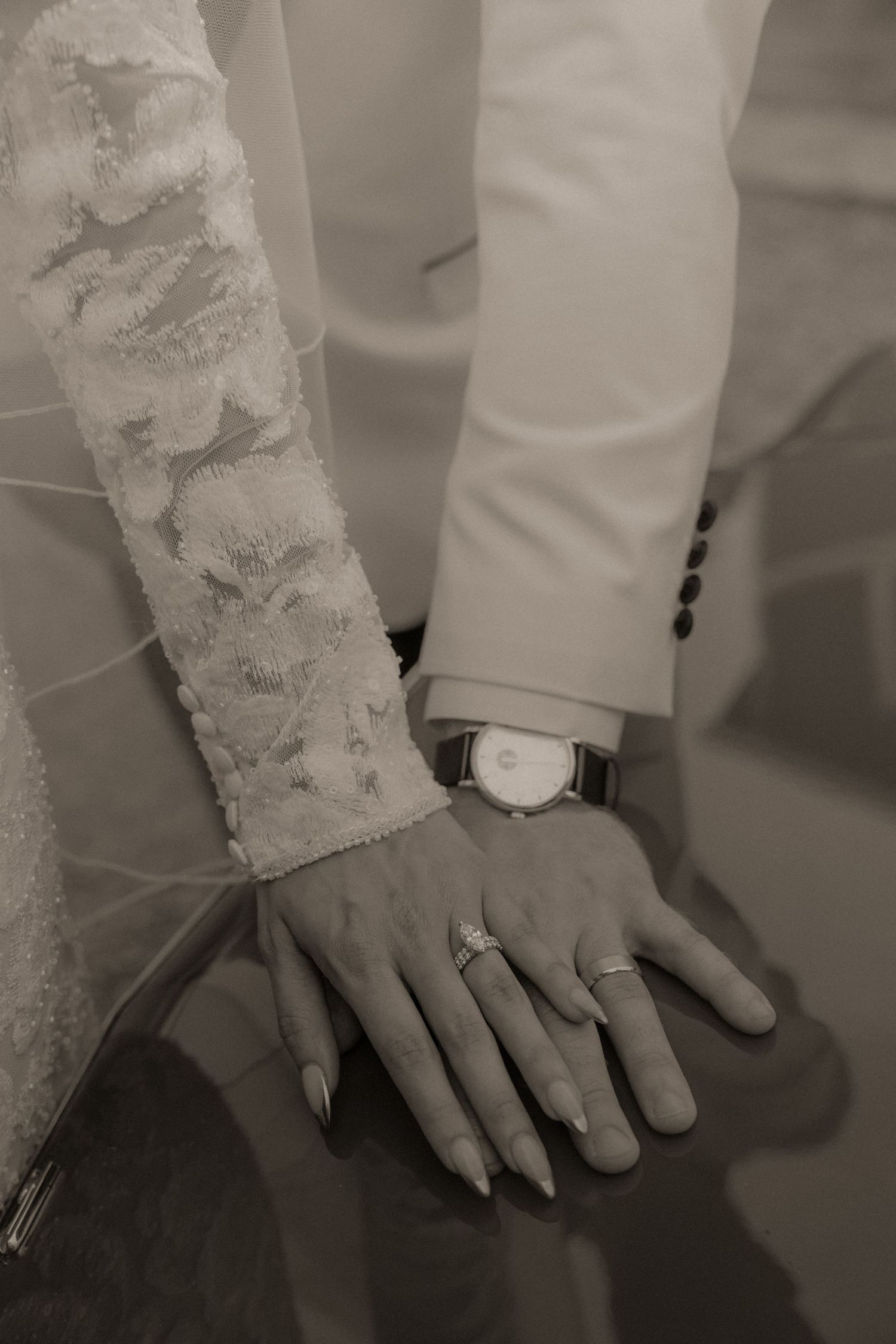 Black and white detail shot of hands with wedding rings and lace sleeve.