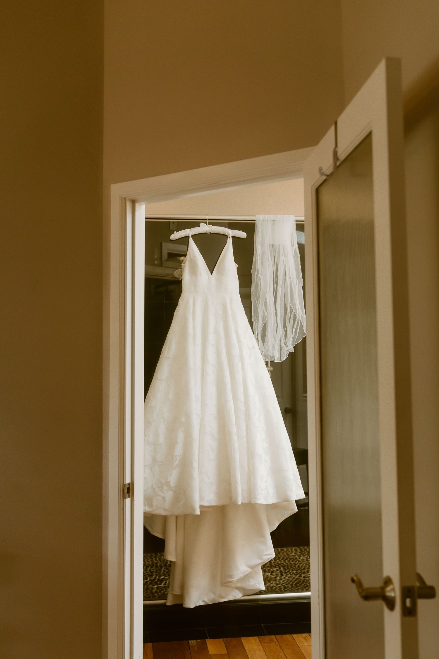 White wedding dress and veil hanging in a doorway on a hanger before the ceremony.