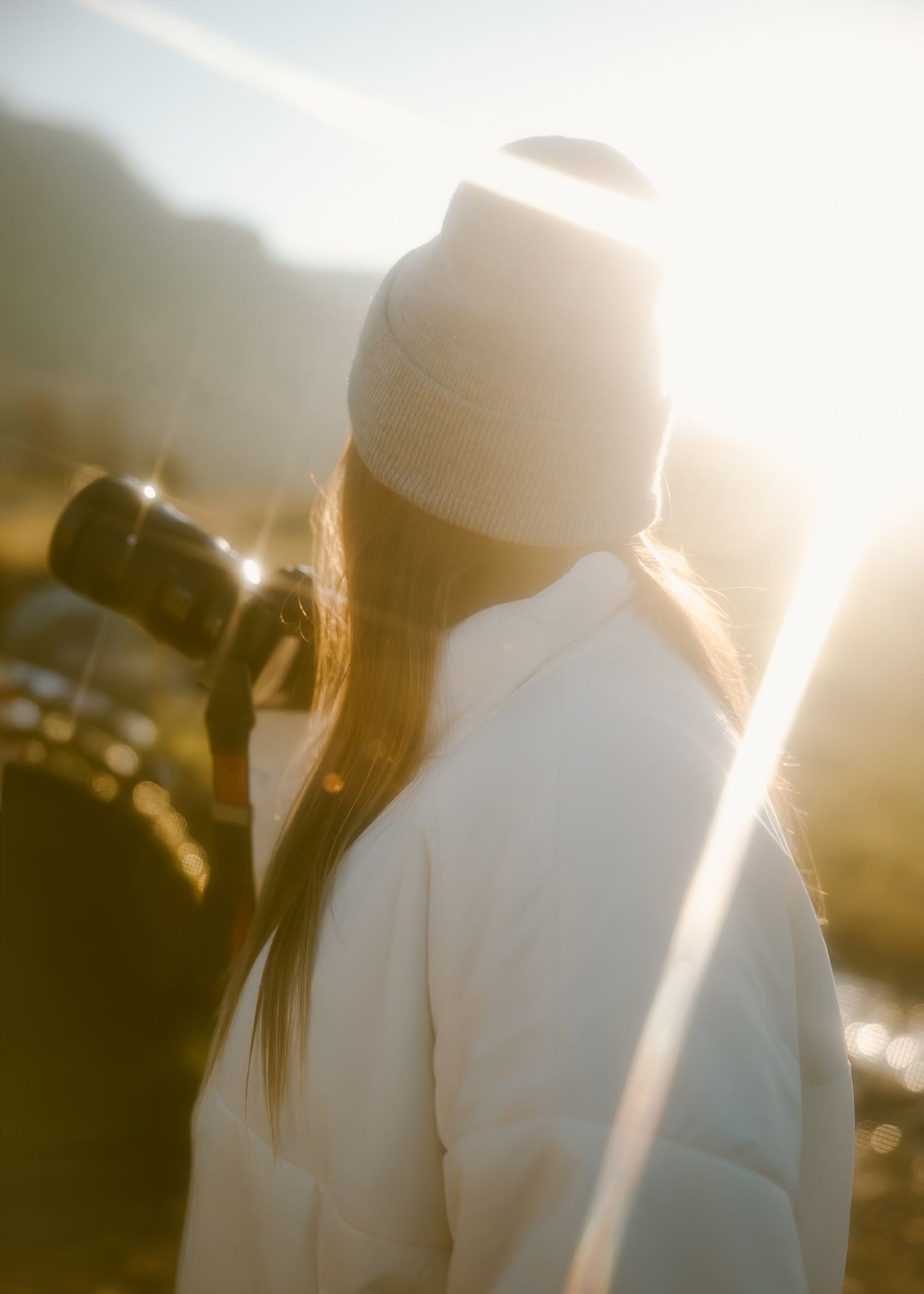 Silhouetted figures in white graduation caps and gowns stand against a bright golden sunset background.