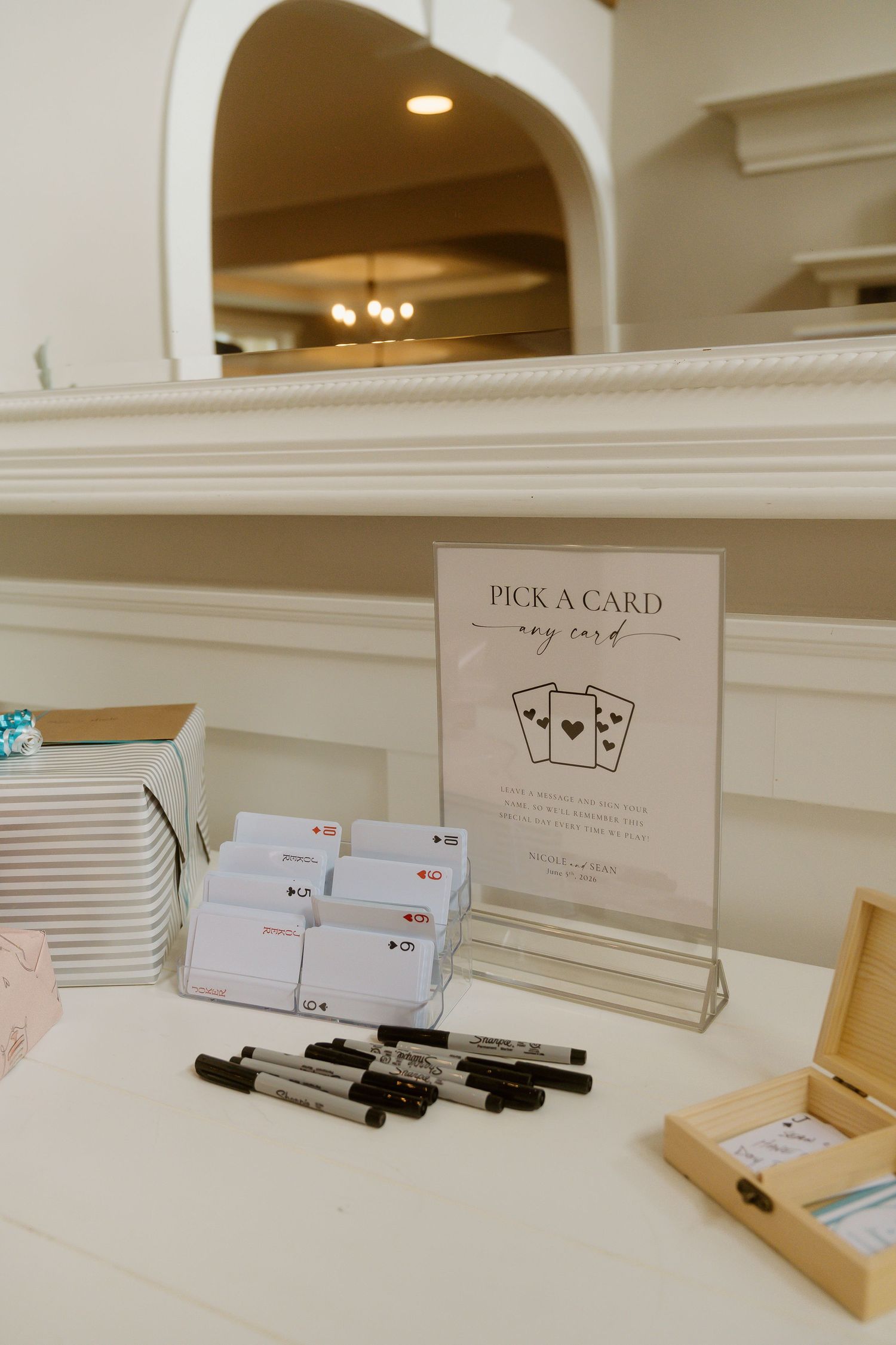Wedding guest book table features Pick A Card display with markers, cards, and wooden keepsake box at elegant reception.