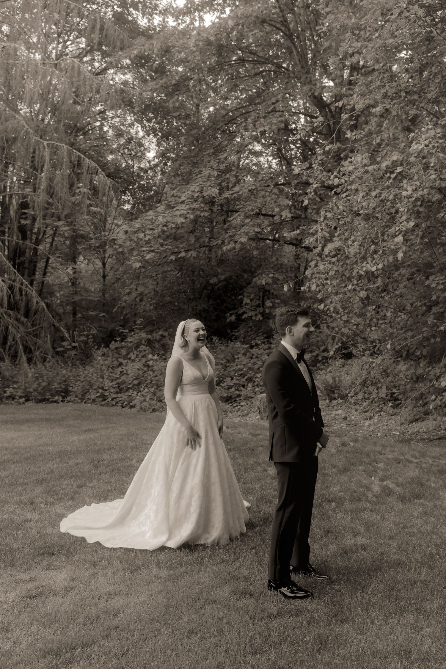 Black and white photo of bride approaching groom during first look in garden.