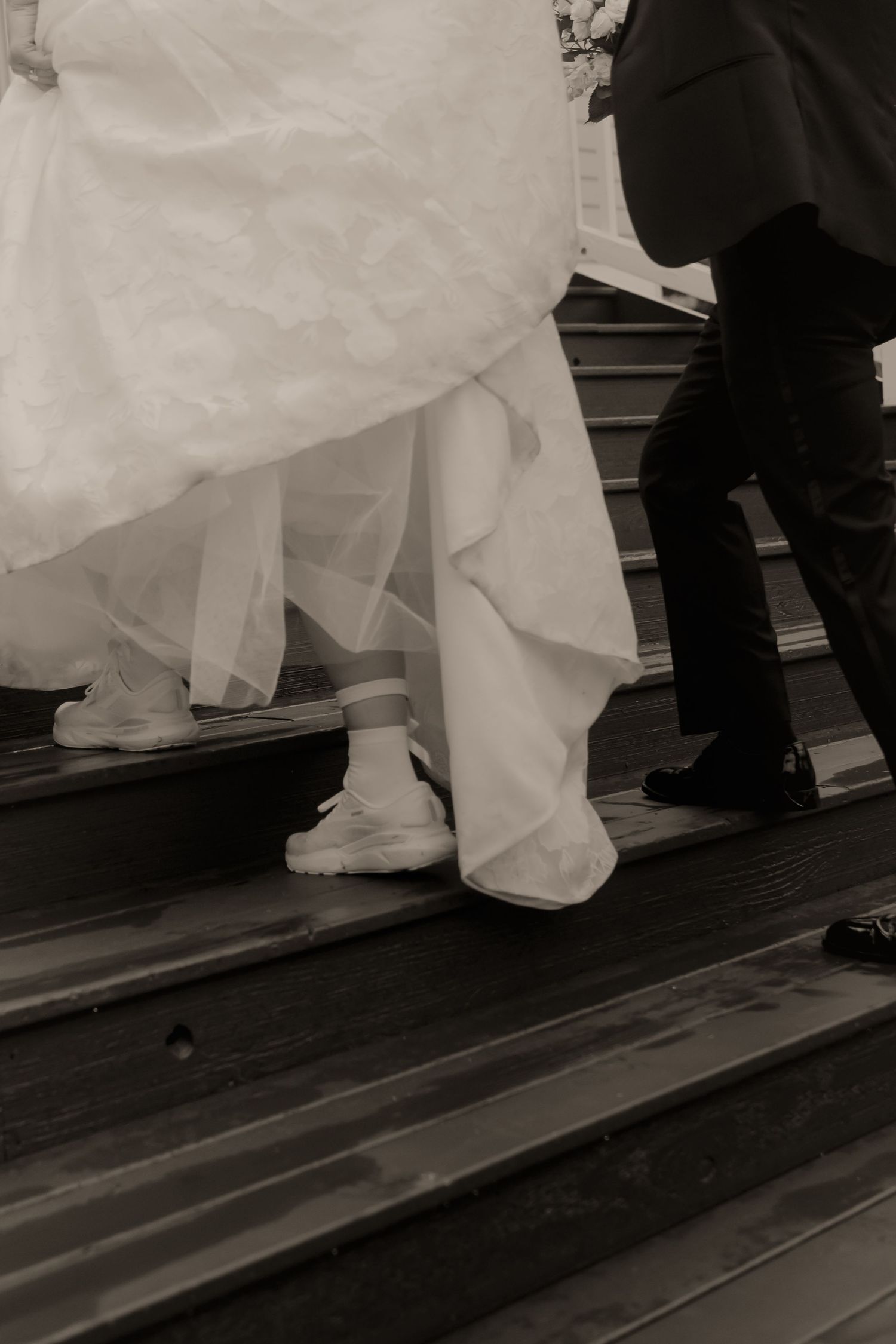 Black and white photo of bride and groom ascending wooden steps, bride wearing white sneakers.