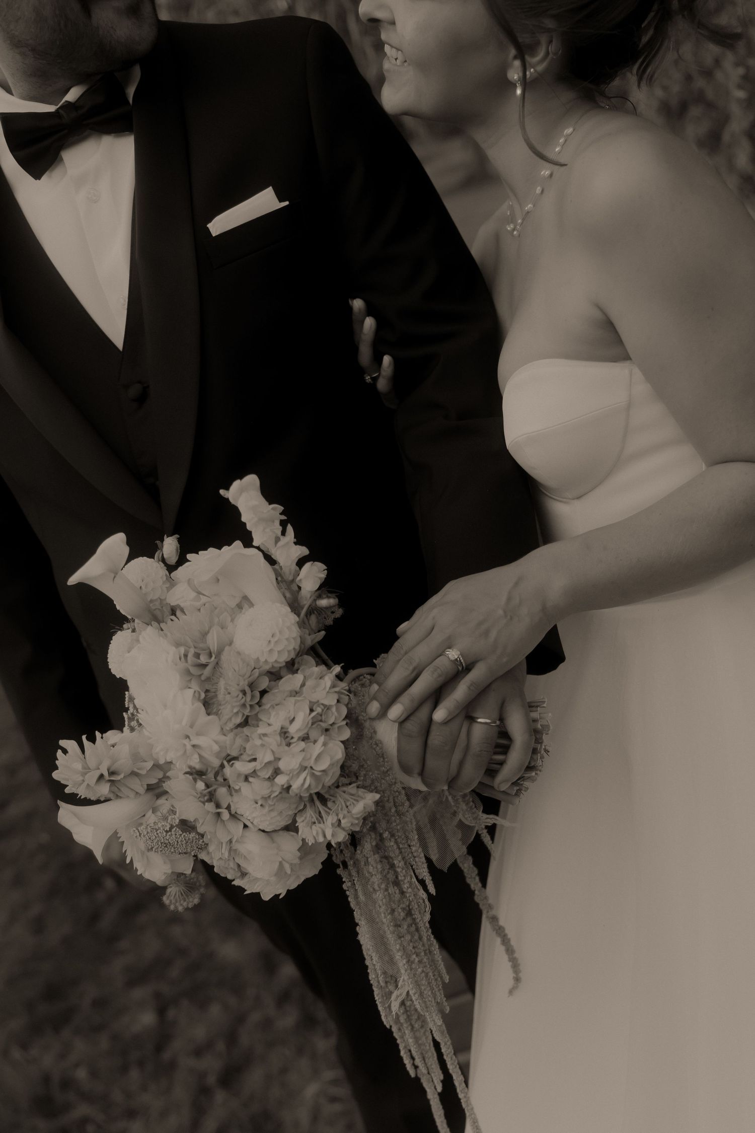Black and white photo of bride and groom holding a floral bouquet together on their wedding day.