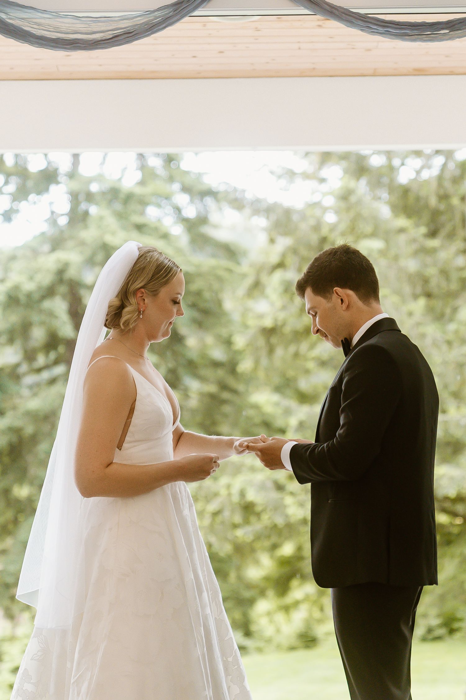 Bride places wedding ring on grooms hand during an intimate outdoor-lit ceremony exchange.