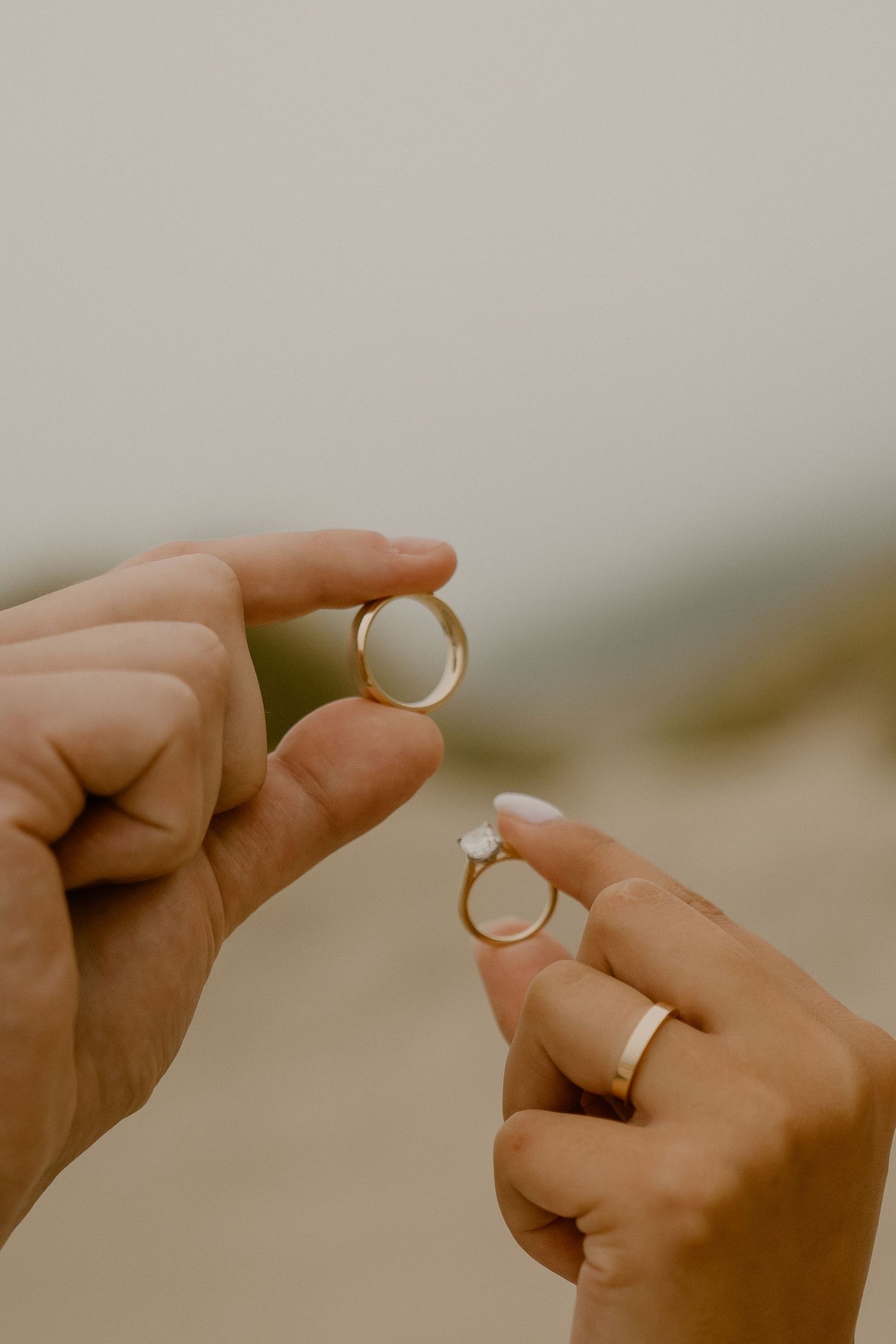 Close-up of hands holding wedding rings against neutral background.