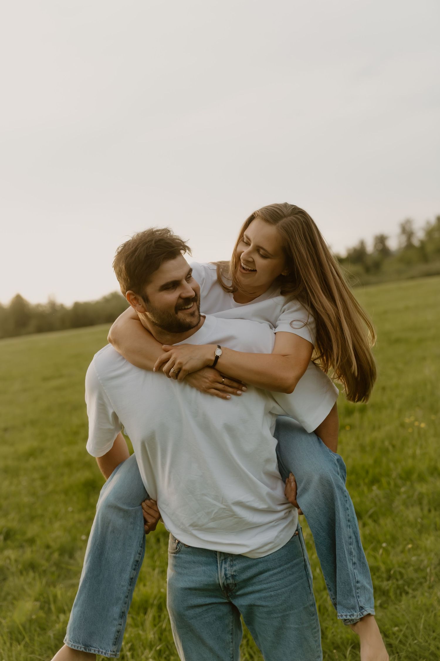 Happy couple laughing outdoors as man gives woman a piggyback ride in a green grassy field.
