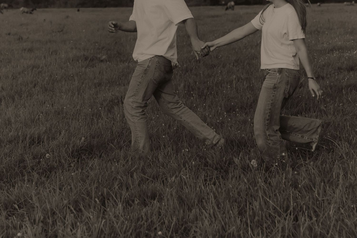 A couple holds hands while running through a grassy field in a romantic black and white outdoor photo.