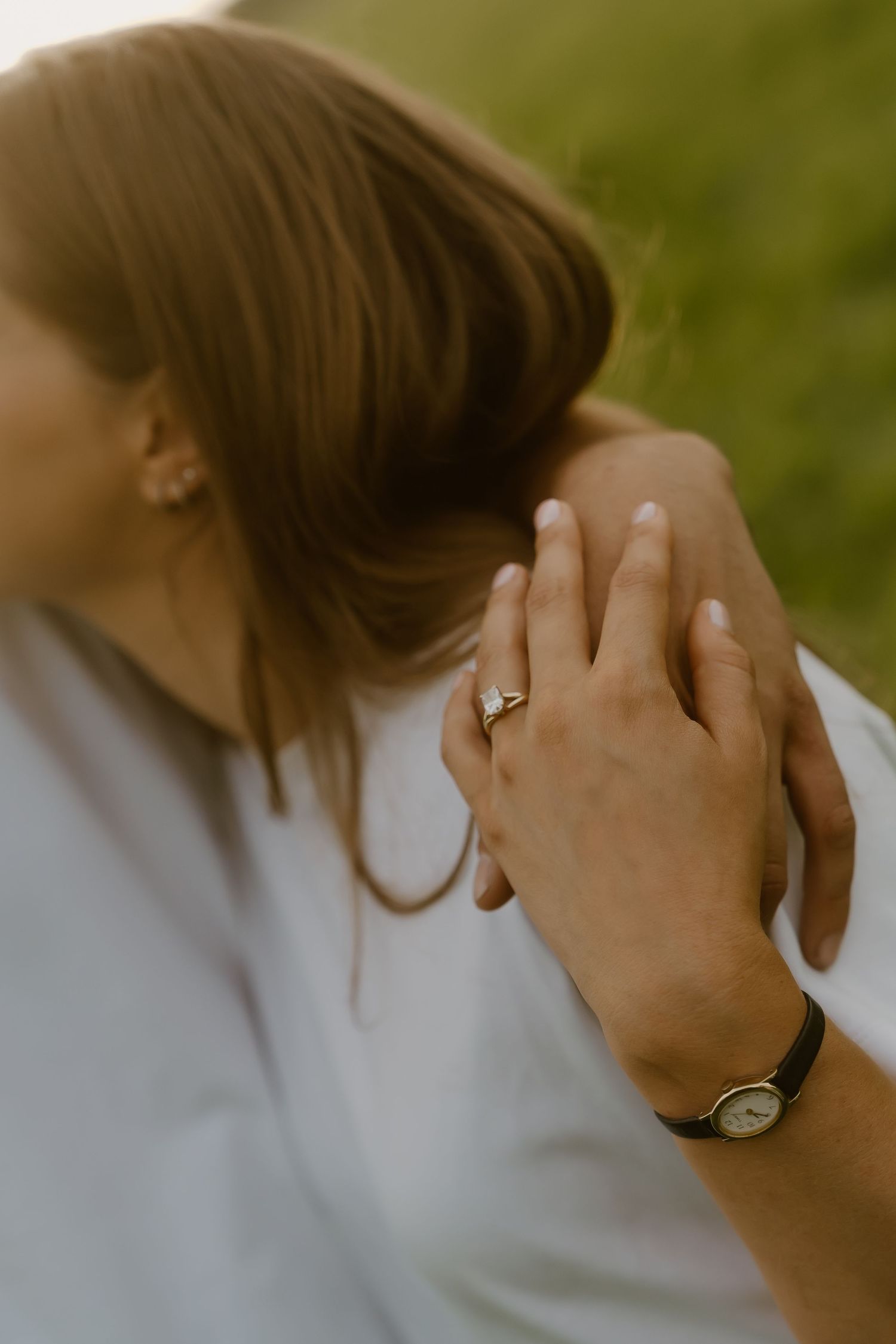 Close-up of woman's hand with engagement ring and man's hand with watch embracing outdoors.