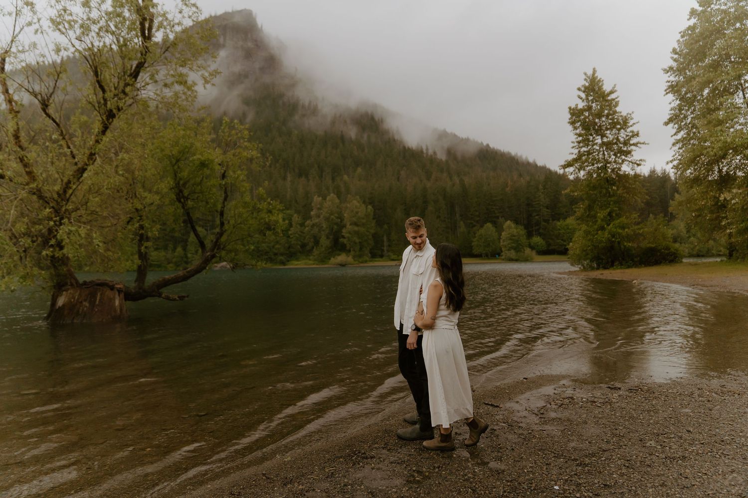 Couple sharing a special moment by a lake with mountains shrouded in fog.