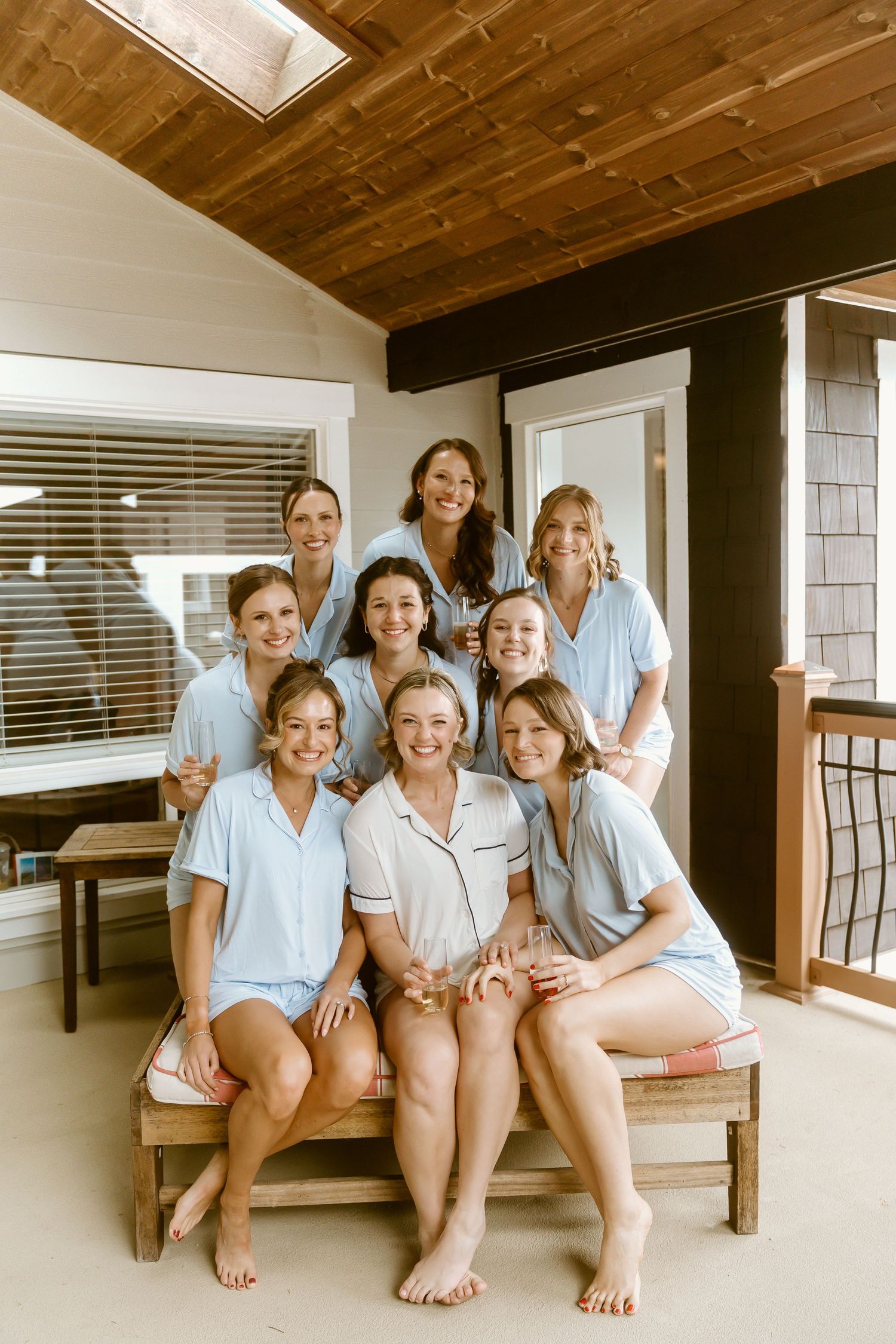 Bride and bridesmaids smiling in matching blue pajamas on a wooden porch.