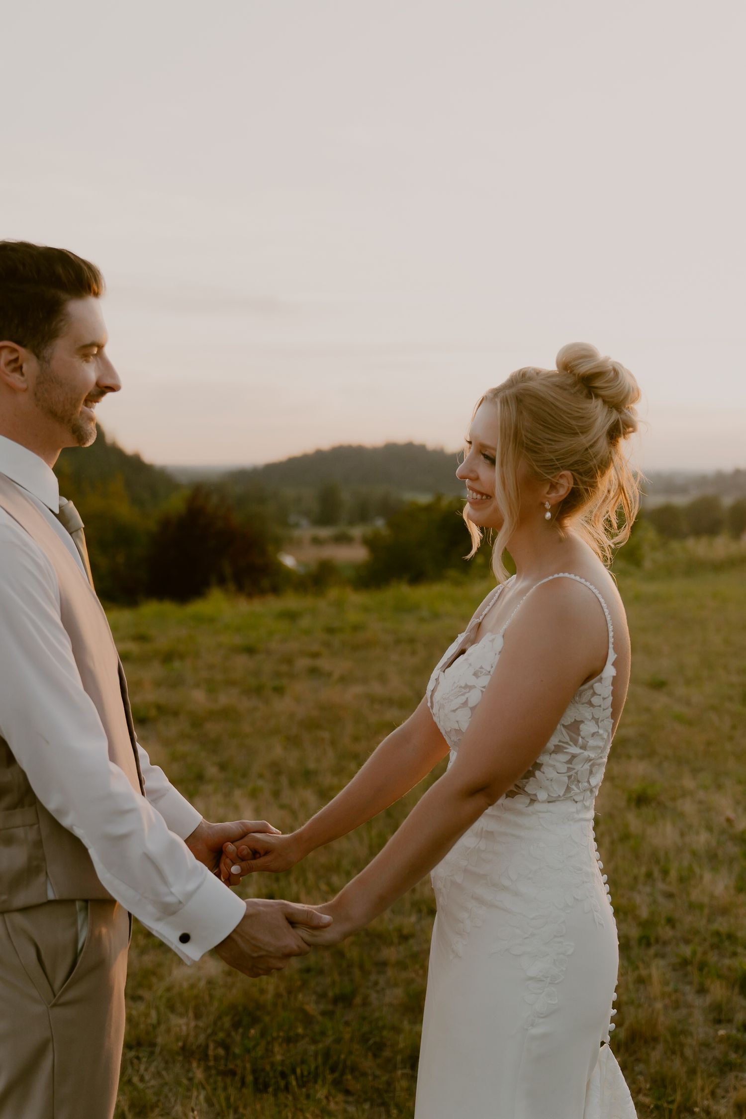 A couple shares a tender moment during their outdoor wedding ceremony in a scenic field at sunset.