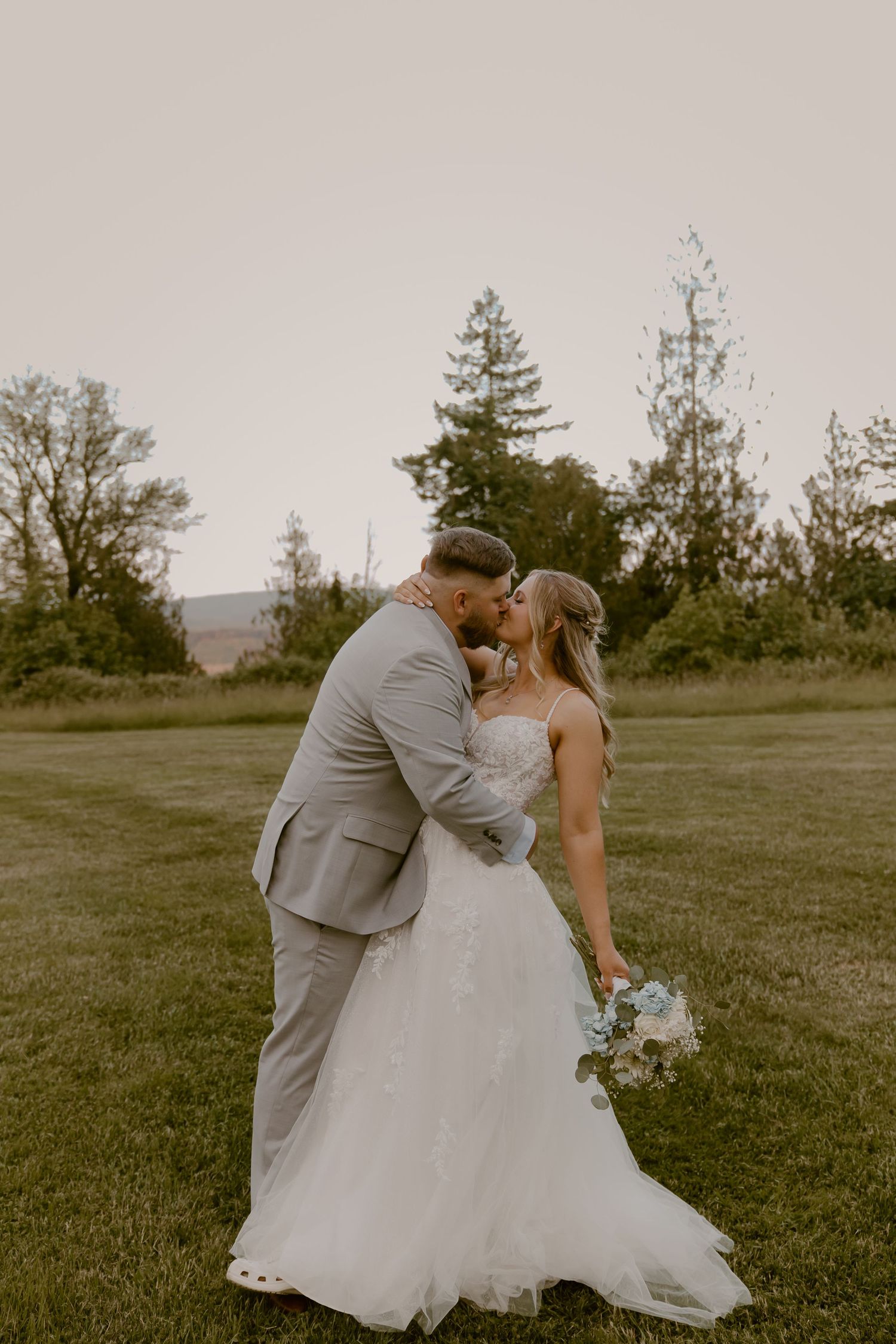 Intimate wedding portrait in field with evergreen trees at golden hour.
