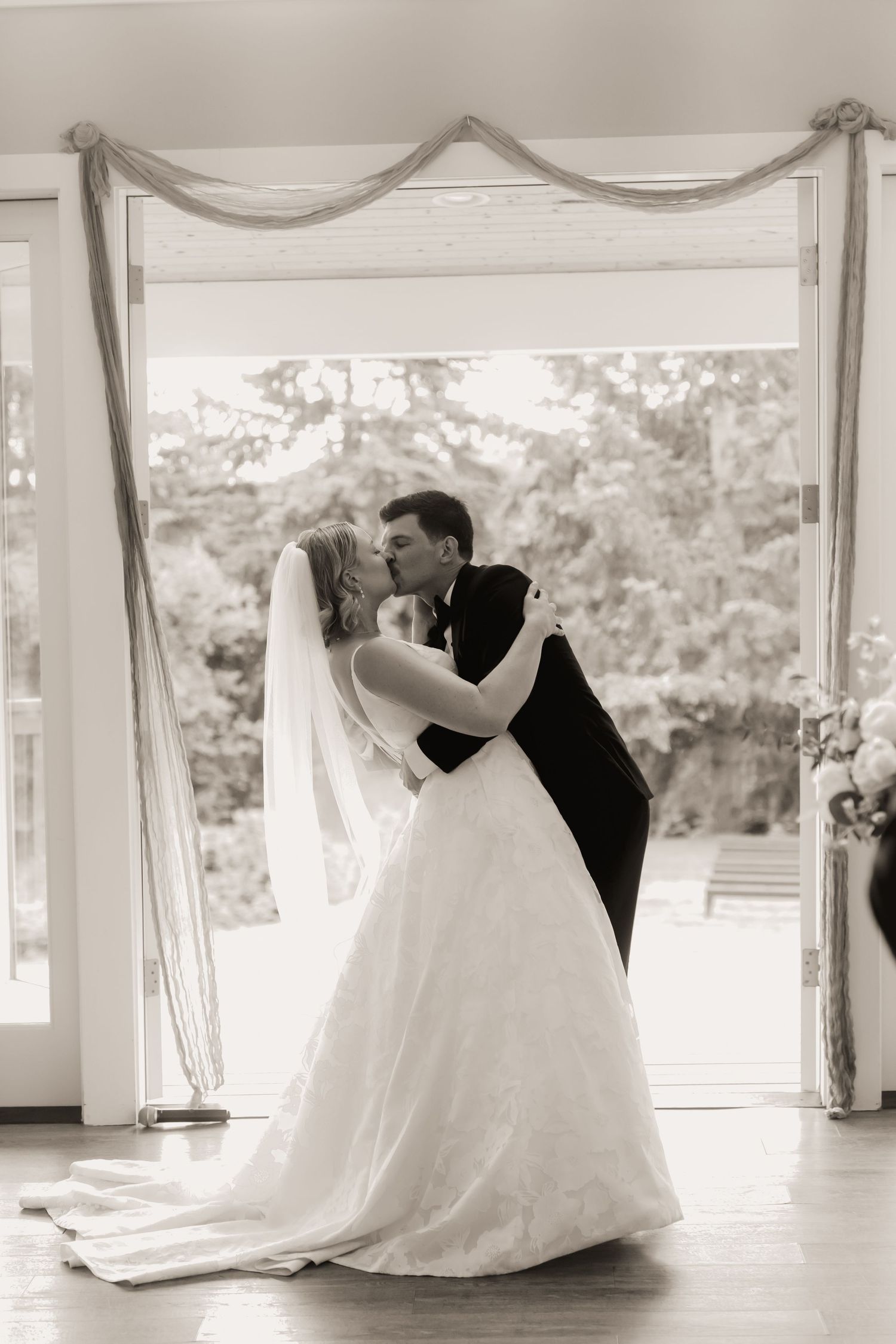 Bride and groom share their first kiss in a black and white wedding ceremony portrait.