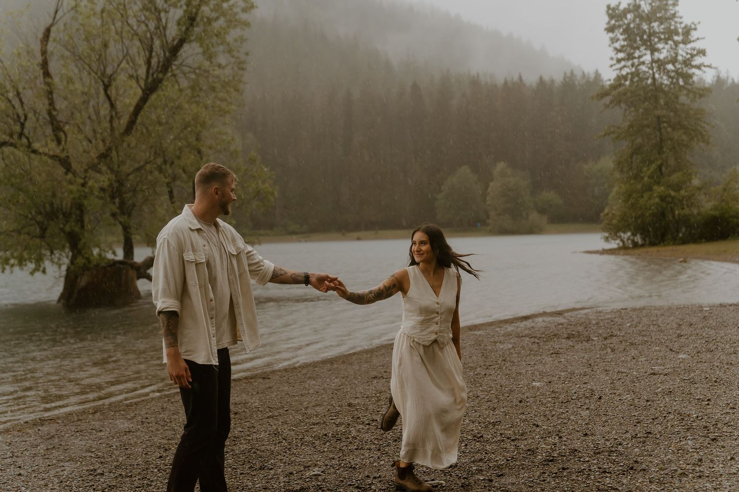 A romantic couple shares intimate moments on a misty beach during a moody photoshoot.