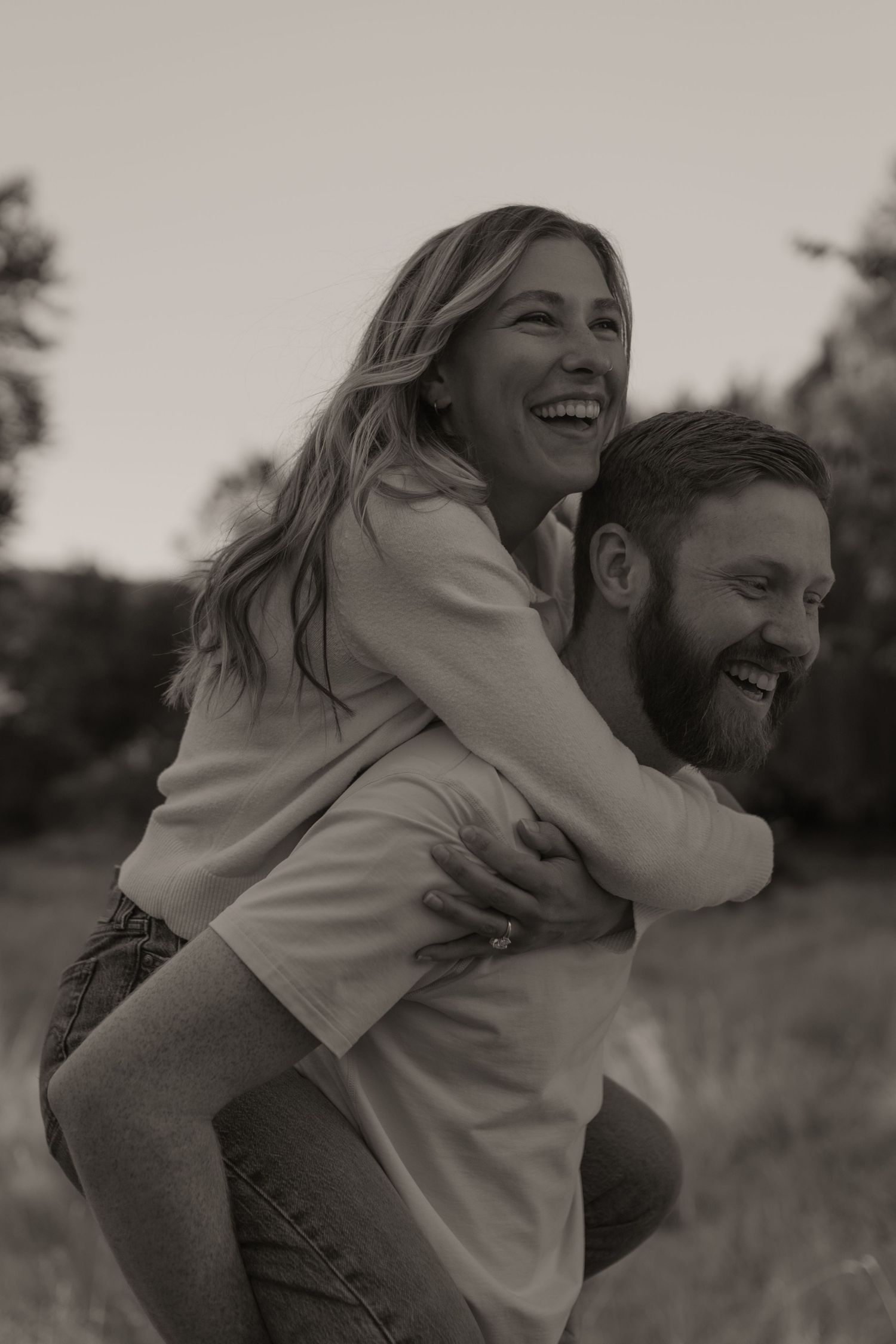 A joyful couple shares playful piggyback moments in black and white photography.