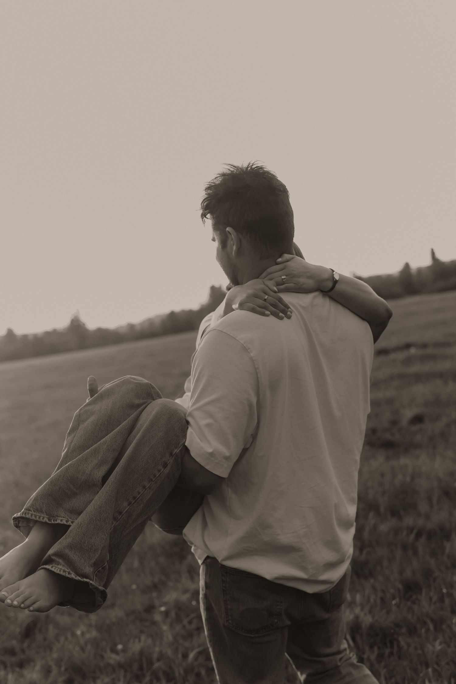 Man carrying woman in his arms across an open field, captured in vintage sepia tone.