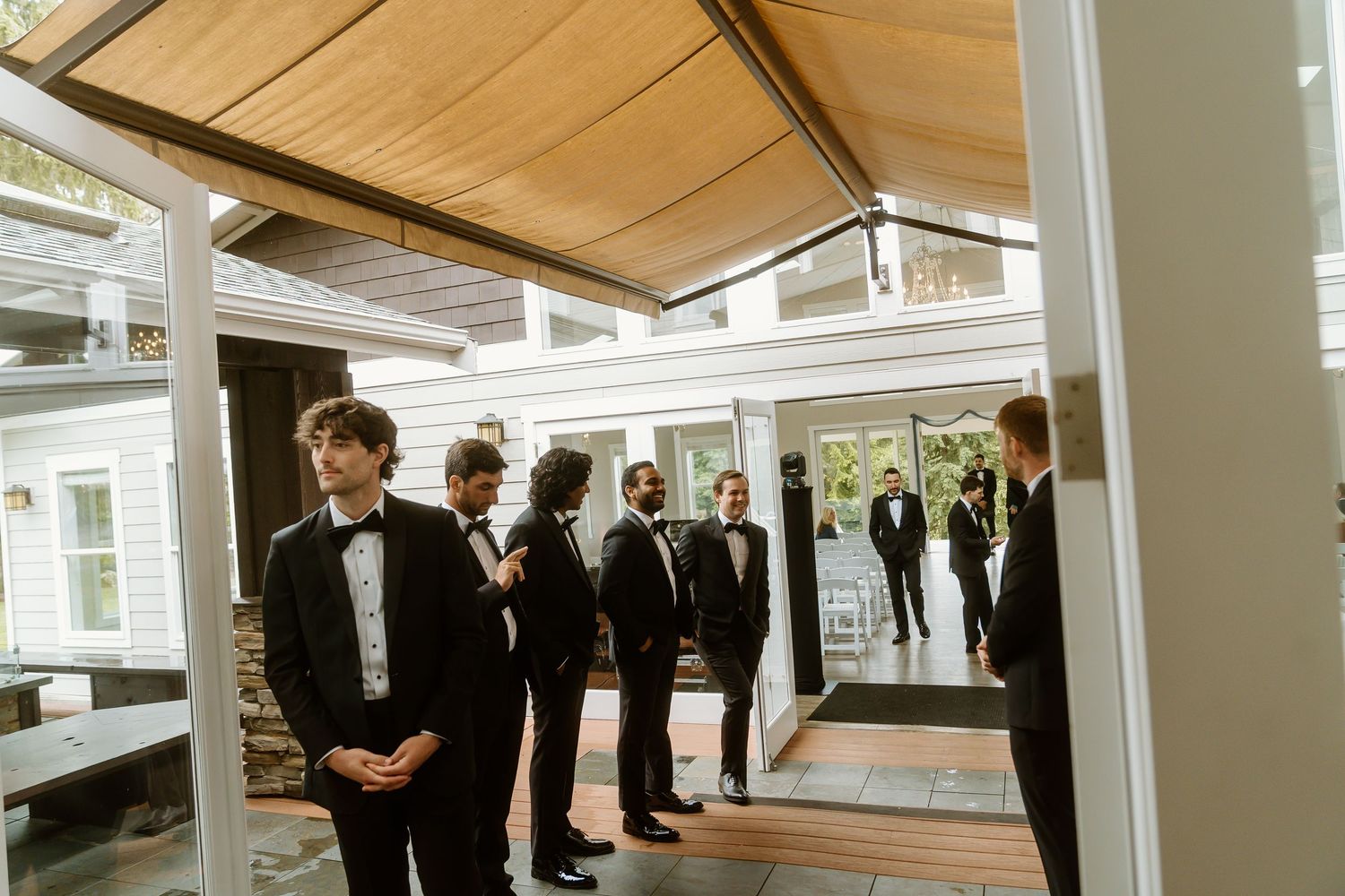 Groomsmen in black tuxedos gathered outside a modern wedding venue before the ceremony.