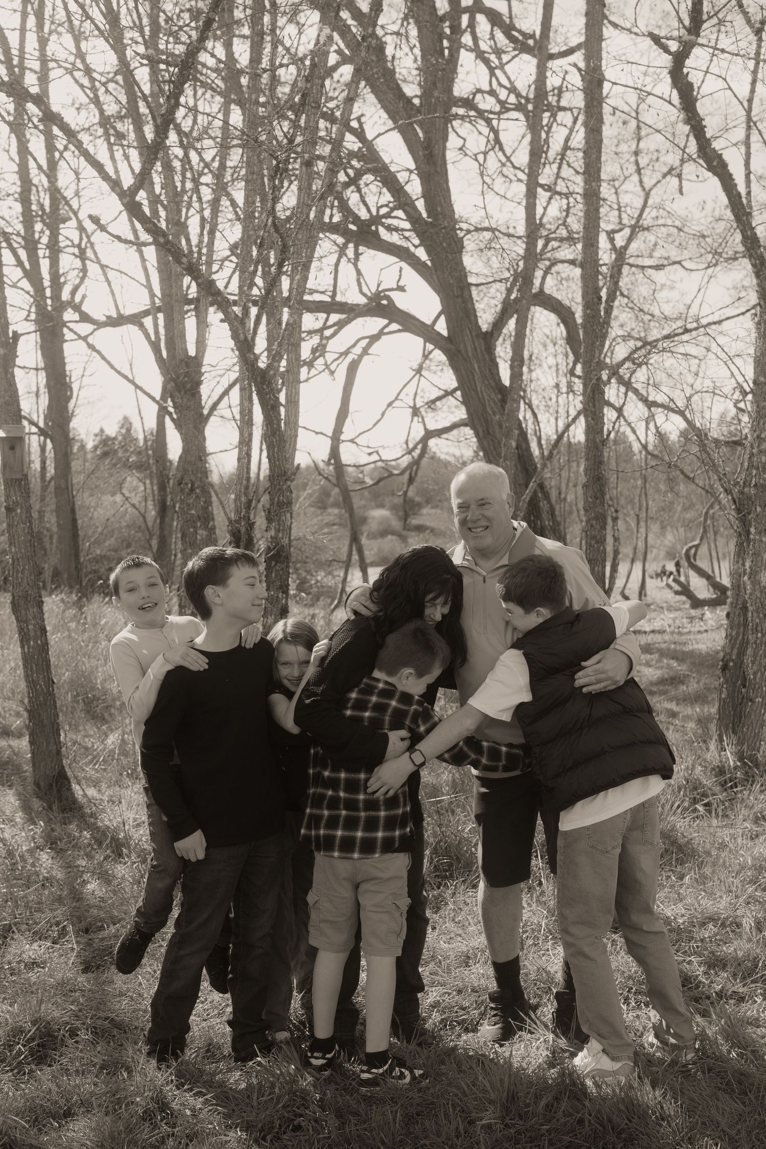 Black and white family photo of grandparents hugging children in a wooded outdoor setting.