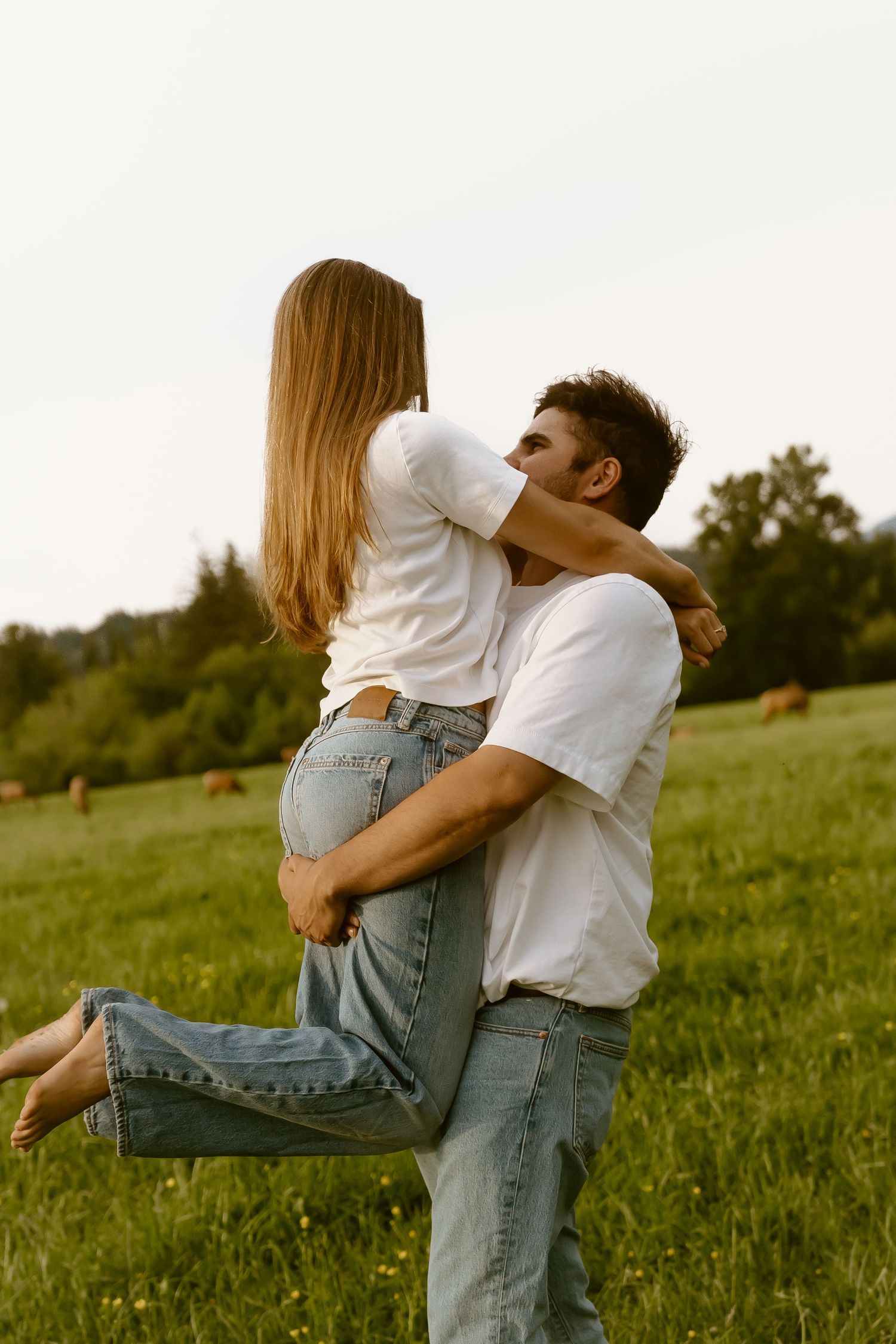 Couple in matching white tees and jeans sharing a romantic kiss in a lush green field.