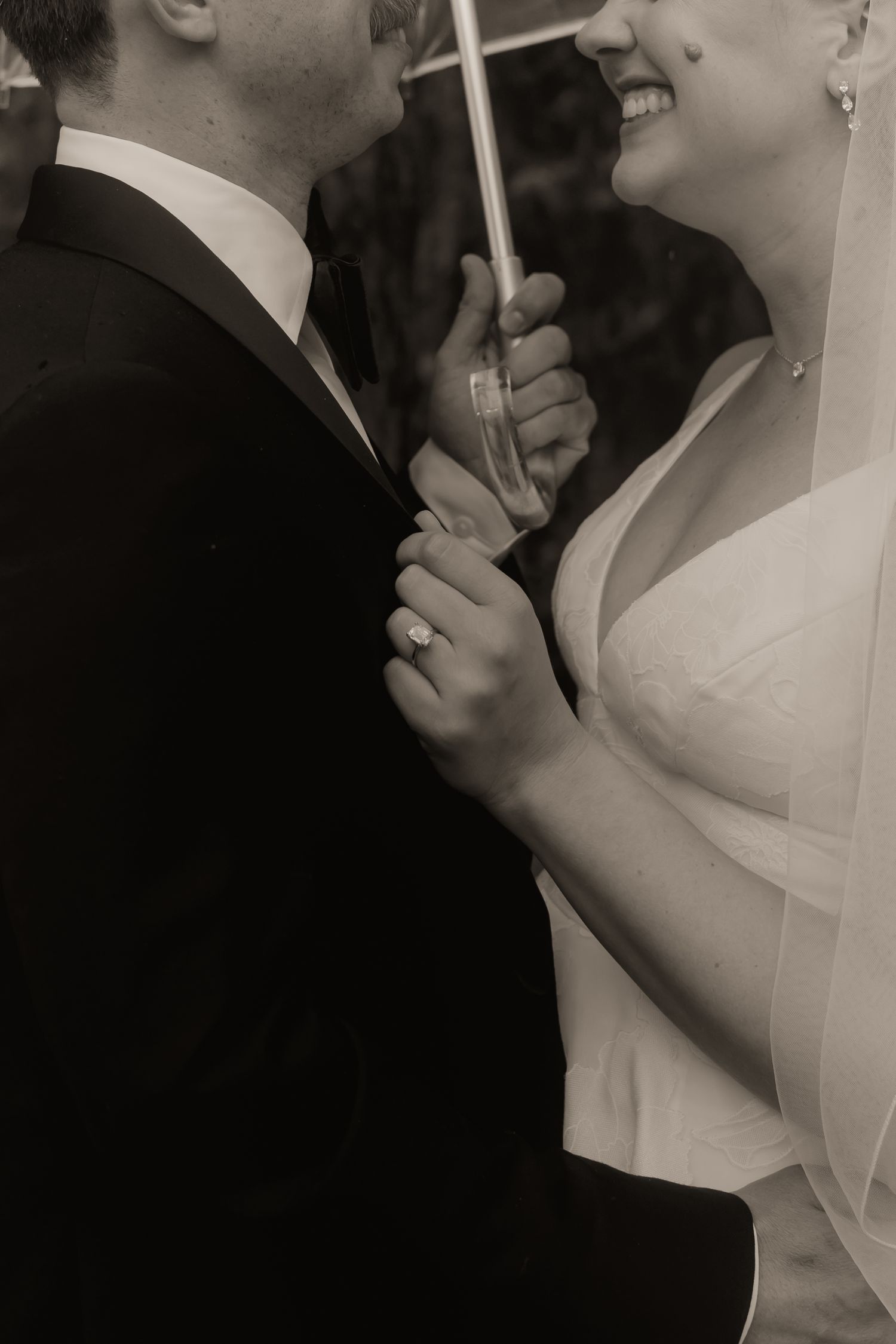 Black and white photo of a bride and groom dancing together under an umbrella, bride smiling and wearing a veil.