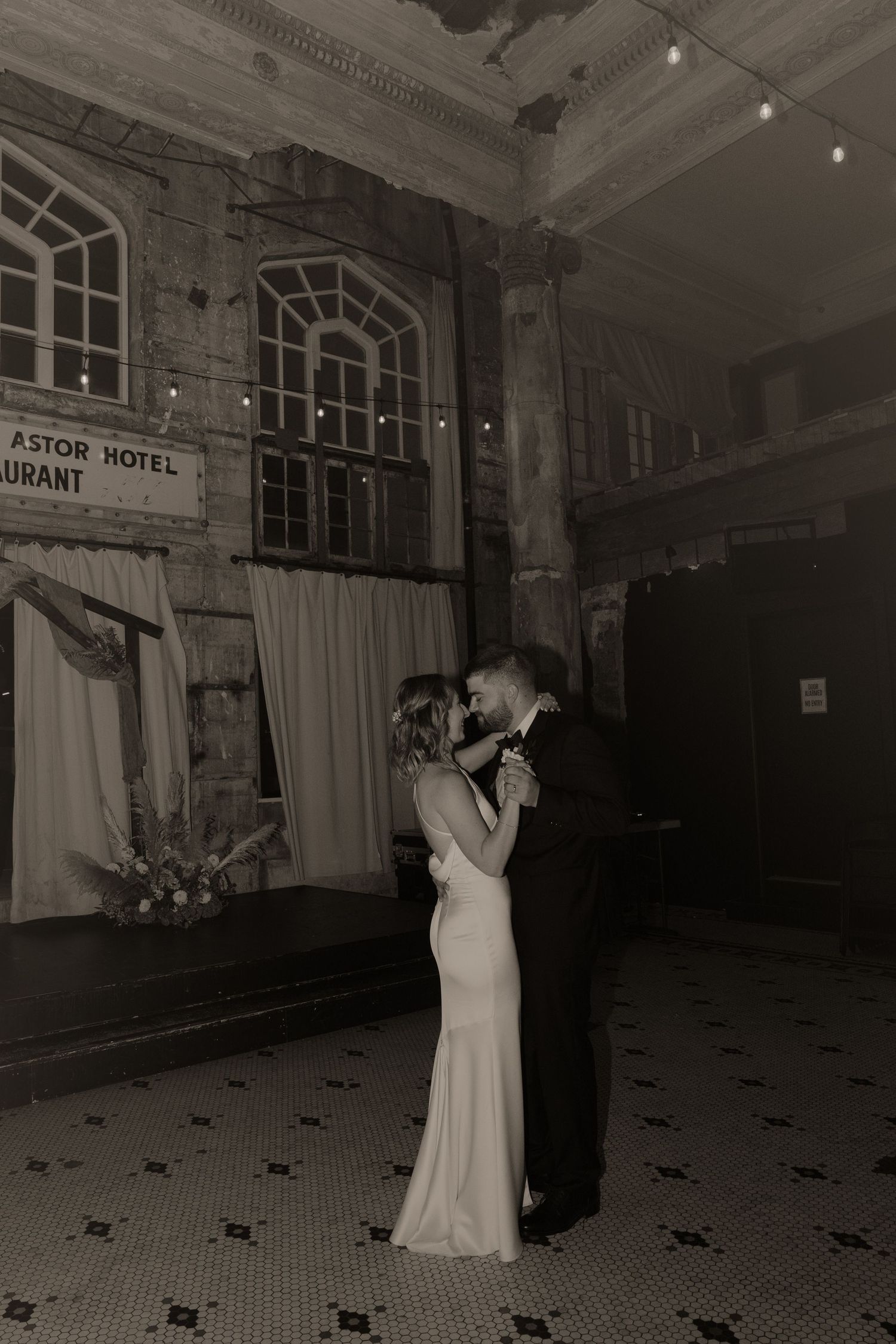A couple dances together in formal attire at the historic Astor Hotel's elegant ballroom with tiled floors and ornate decor.