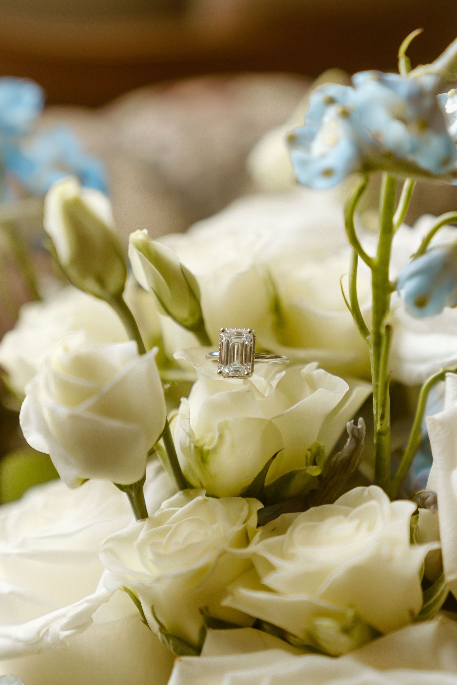Diamond engagement ring nestled among white roses and blue flowers in a bridal bouquet.