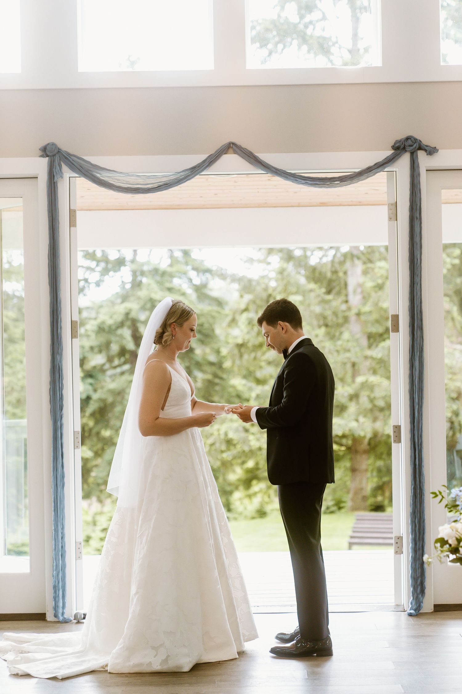 Bride places a wedding ring on the grooms finger during an elegant indoor ceremony.