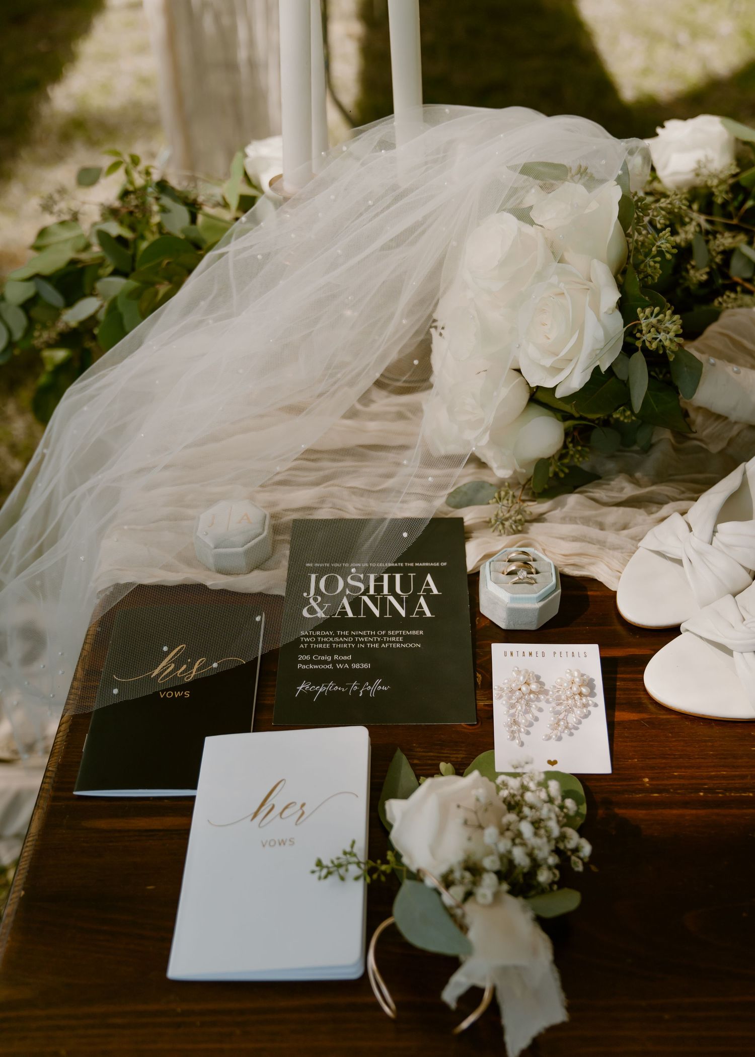 Wedding stationery with vow books, invitations and white floral decorations on wooden table with flowing tulle veil.