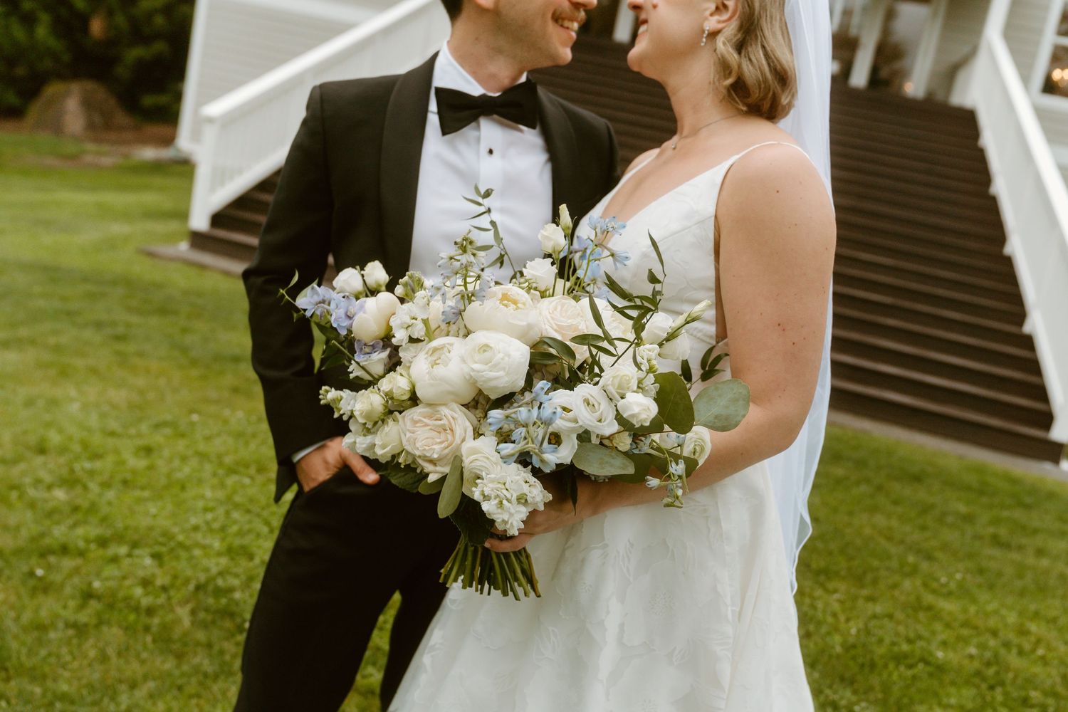 Bride and groom share a romantic moment, bride holding white and blue floral bouquet, groom in black tuxedo.