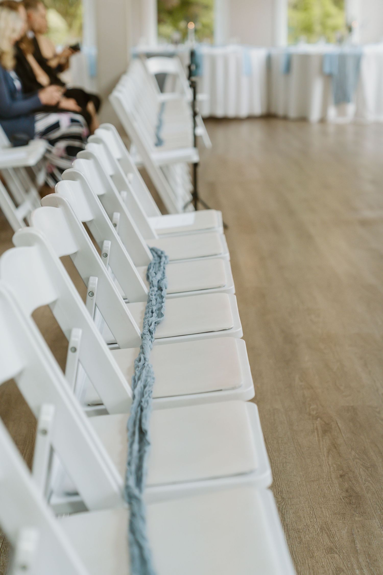 White folding chairs with blue ribbon decorations line the aisle of an elegant wedding venue.