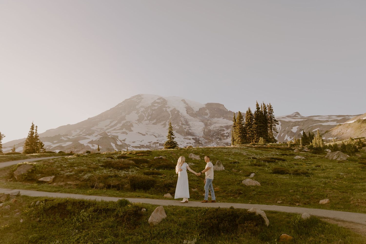 A scenic mountain landscape with a winding road and evergreen trees against a cloudy sky at sunset.