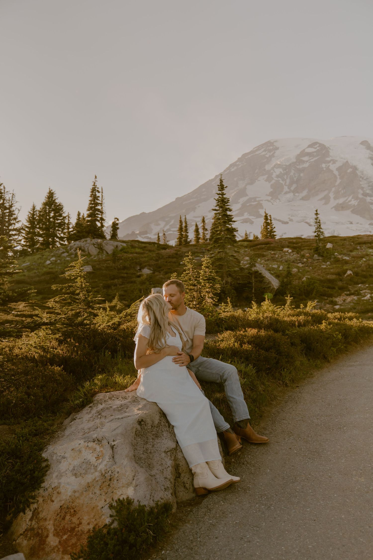 Intimate moment captured on mountain trail with snow-capped peaks in background.